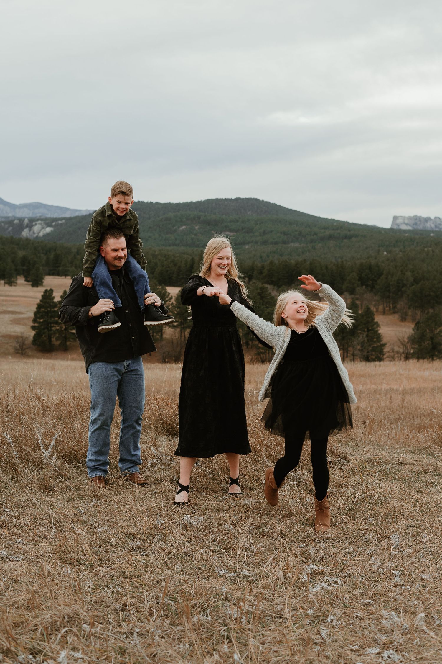 Playful family interaction in an autumn field with mountains visible in the distance.