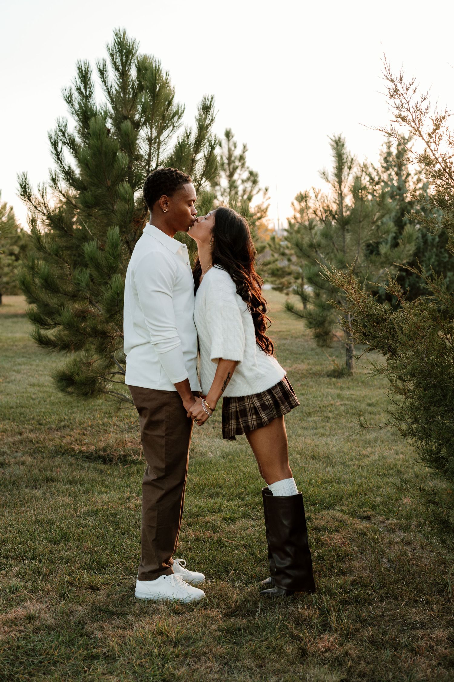 Couple in white and plaid sharing tender moments among pine trees at golden hour.