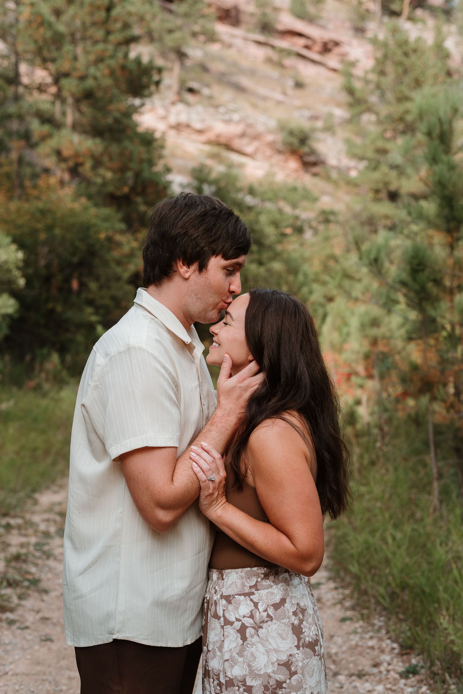 A romantic couple shares tender moments together on a nature trail surrounded by greenery and sunlight.