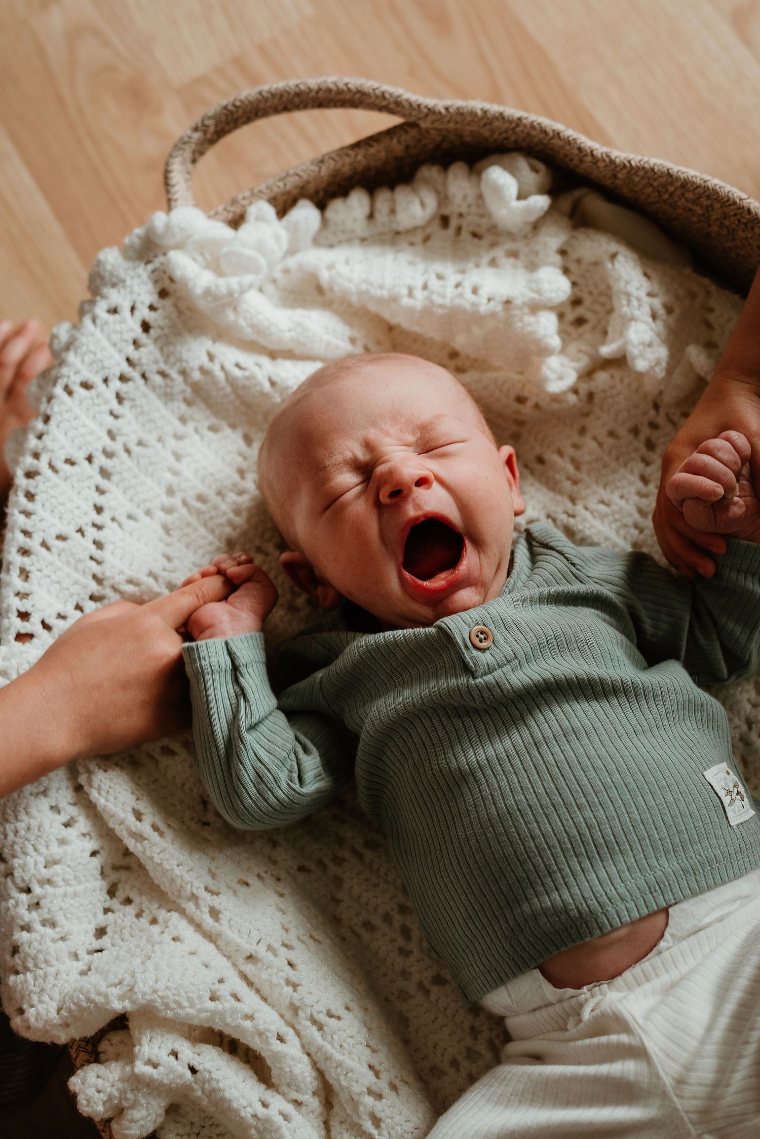 Newborn baby in sage green outfit expressing different emotions while lying on white lace blanket.