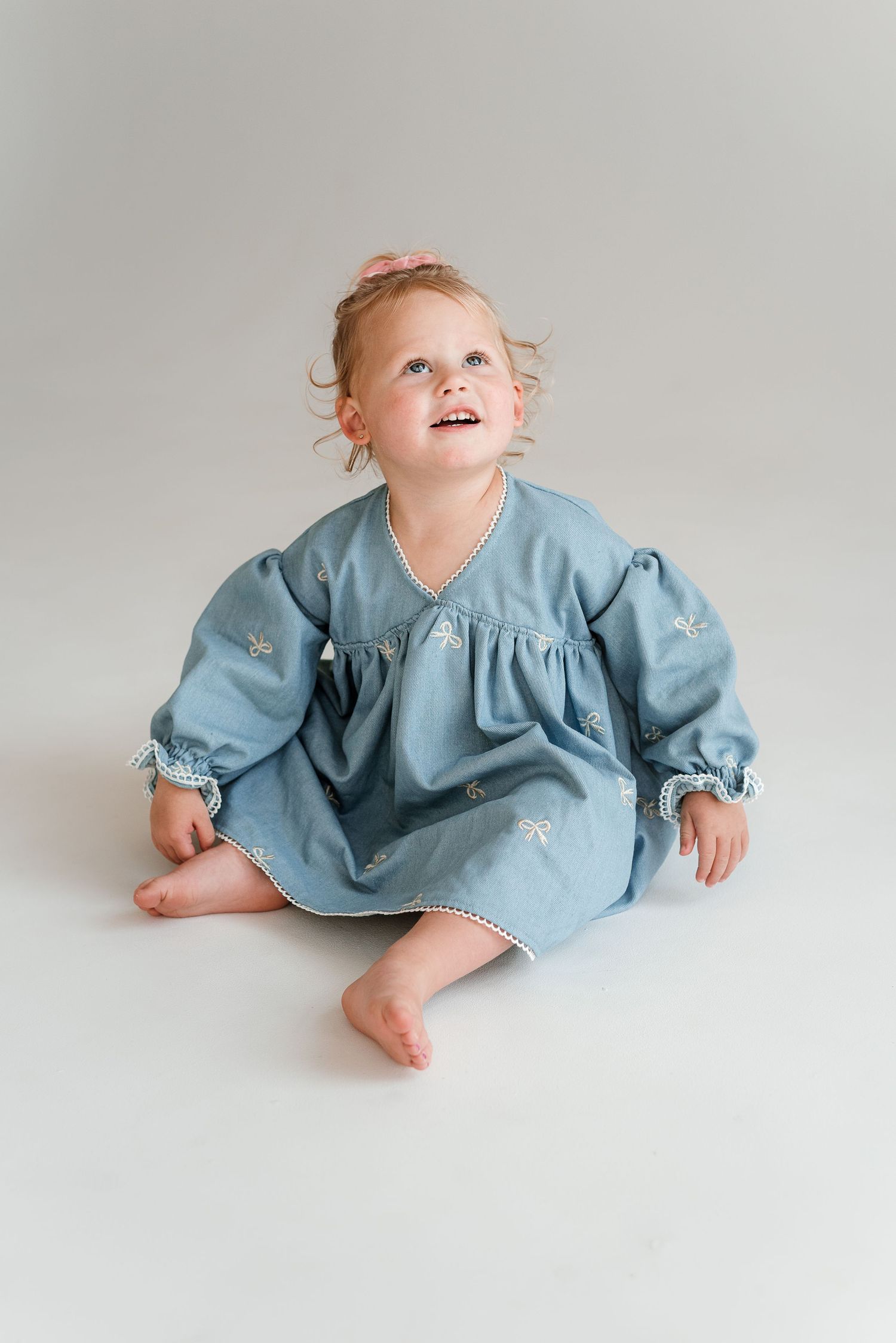 A baby in a blue dress lays on a white background in a series of playful poses.