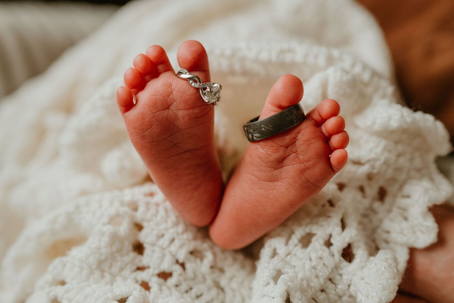 Tiny newborn baby feet resting on delicate white crocheted blanket with intricate pattern details.