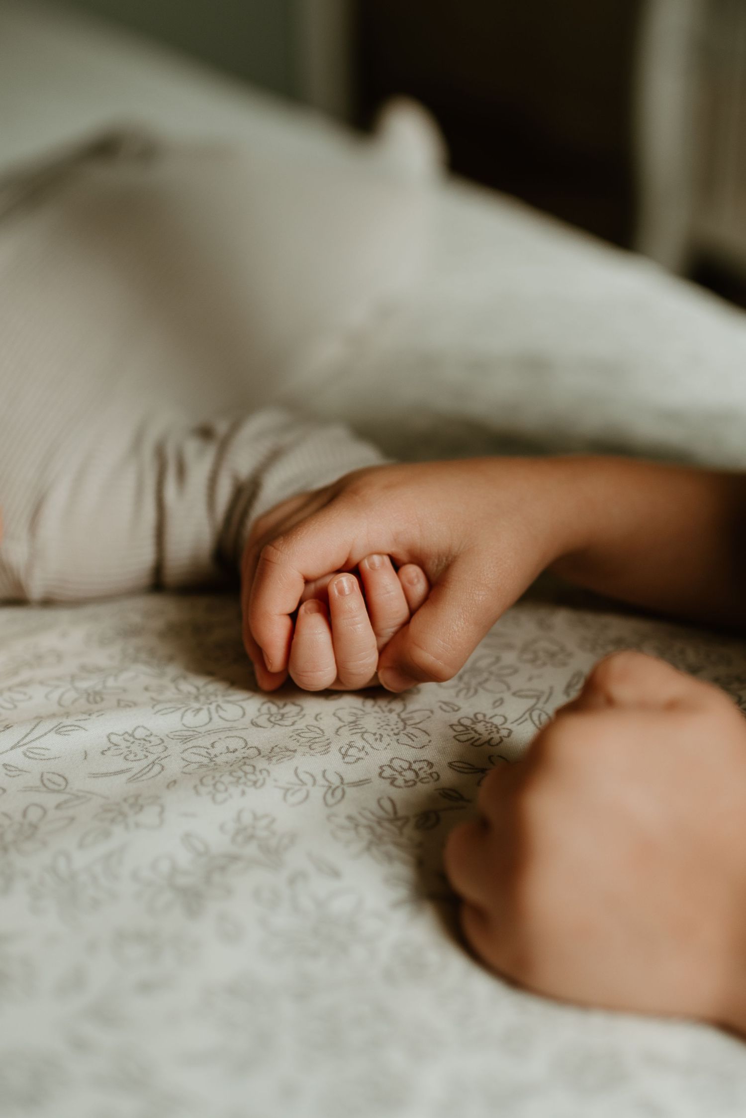 Small baby hands grasp delicately at soft white textured bedding in a tender moment.