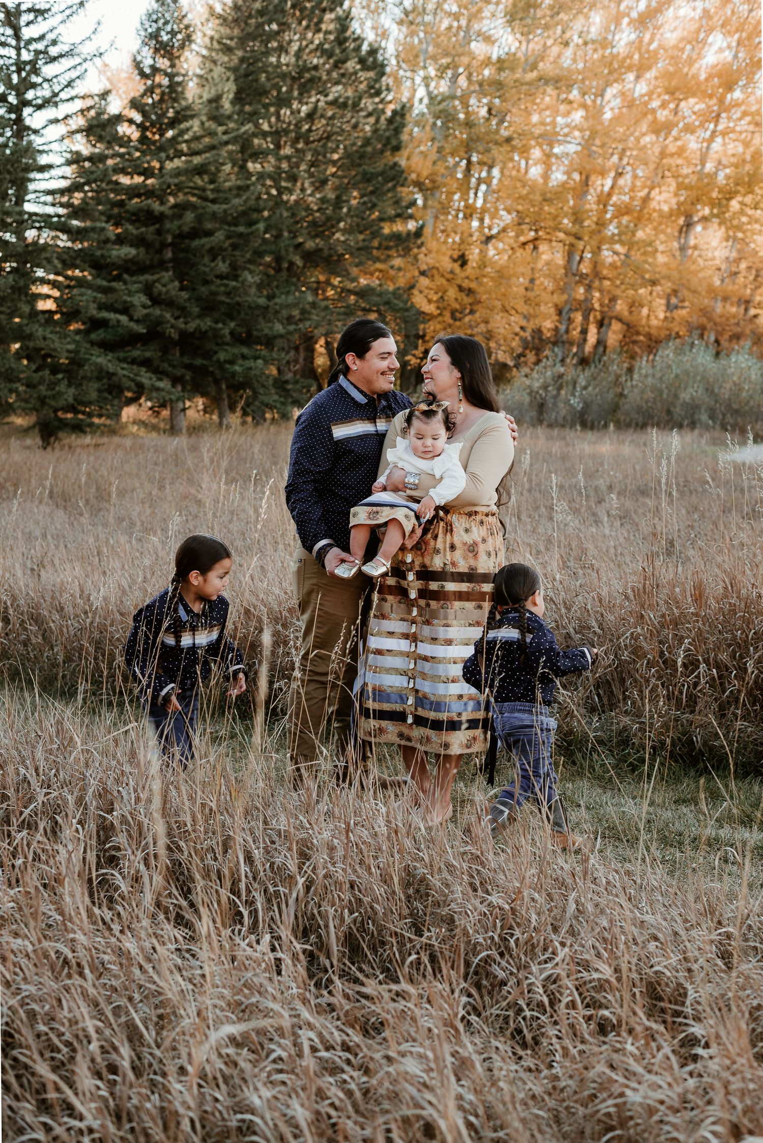 Family sharing intimate moments in tall grass field during golden hour.