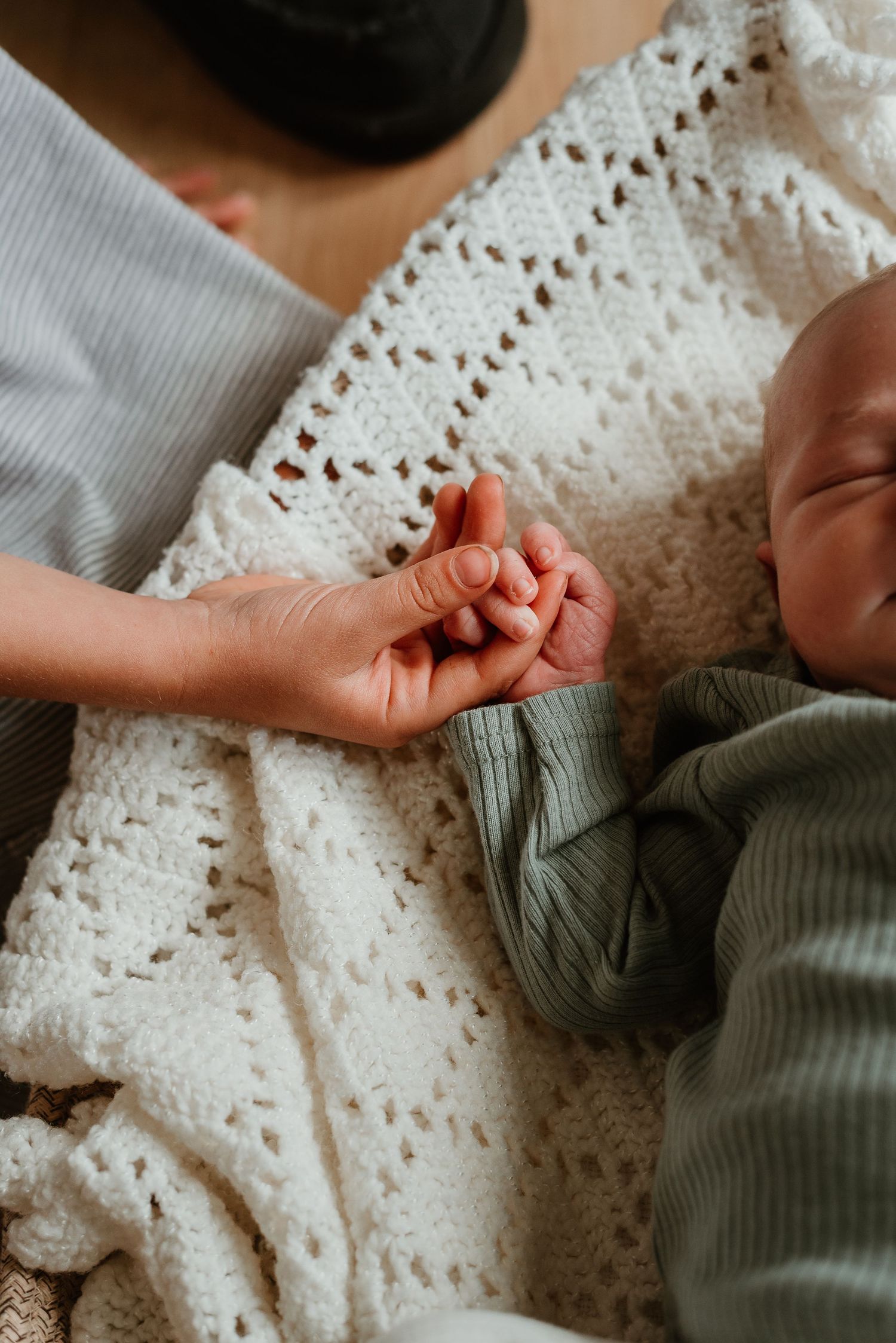 Detail shots of tiny baby hands against white crochet blanket and sage green clothing.