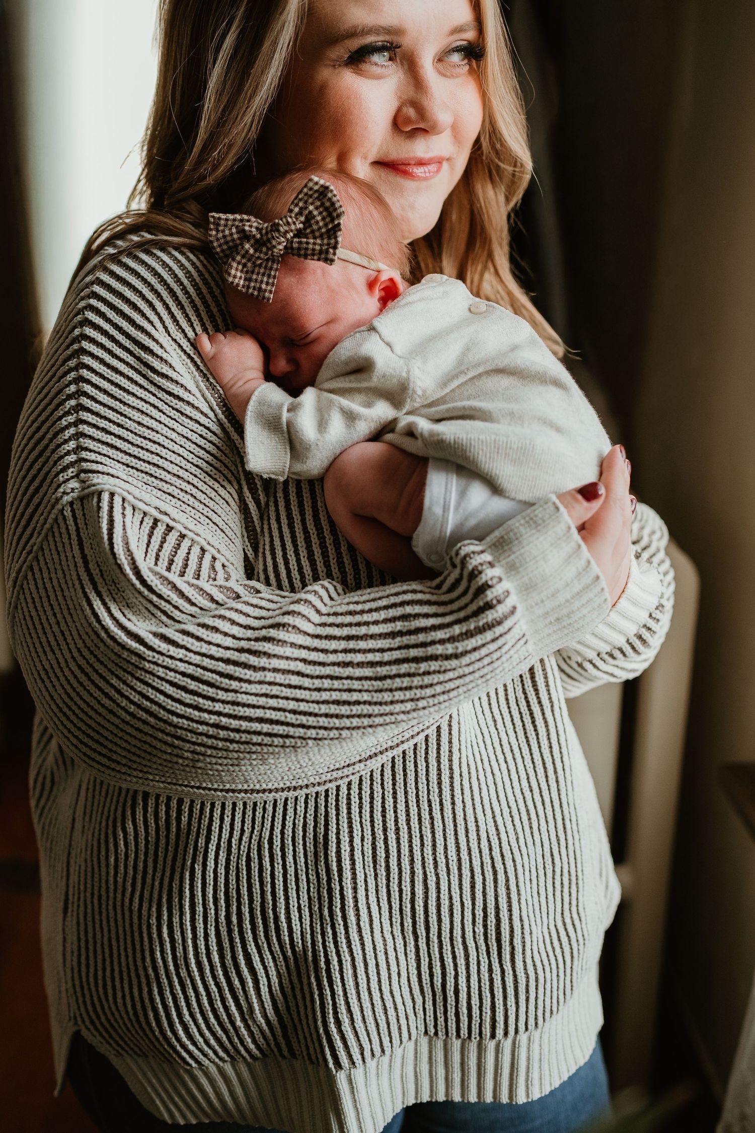 A tender moment captured as someone wearing a cozy striped sweater cradles a newborn baby wrapped in white.