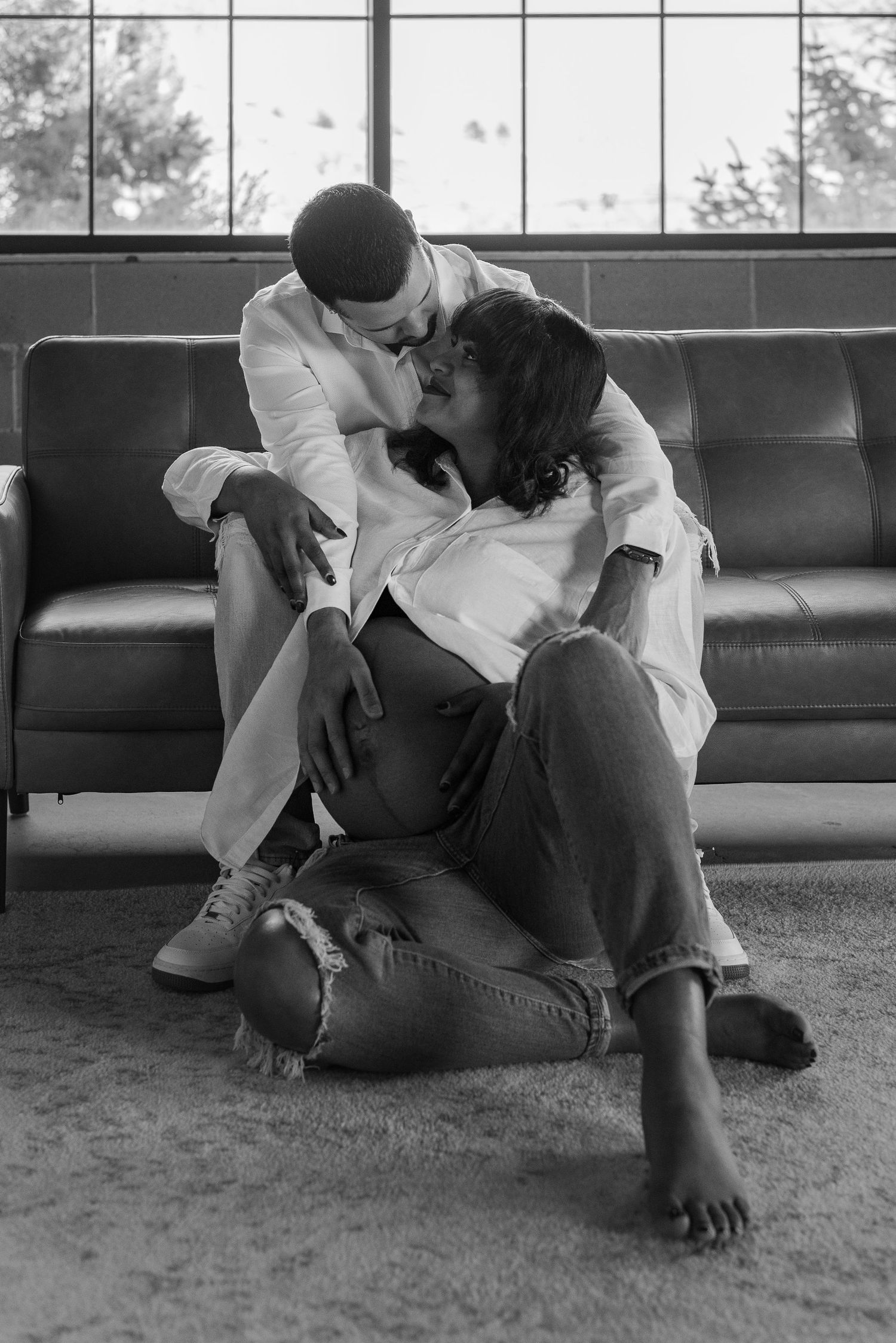 Intimate black and white photo of couple sharing tender moment on leather couch.