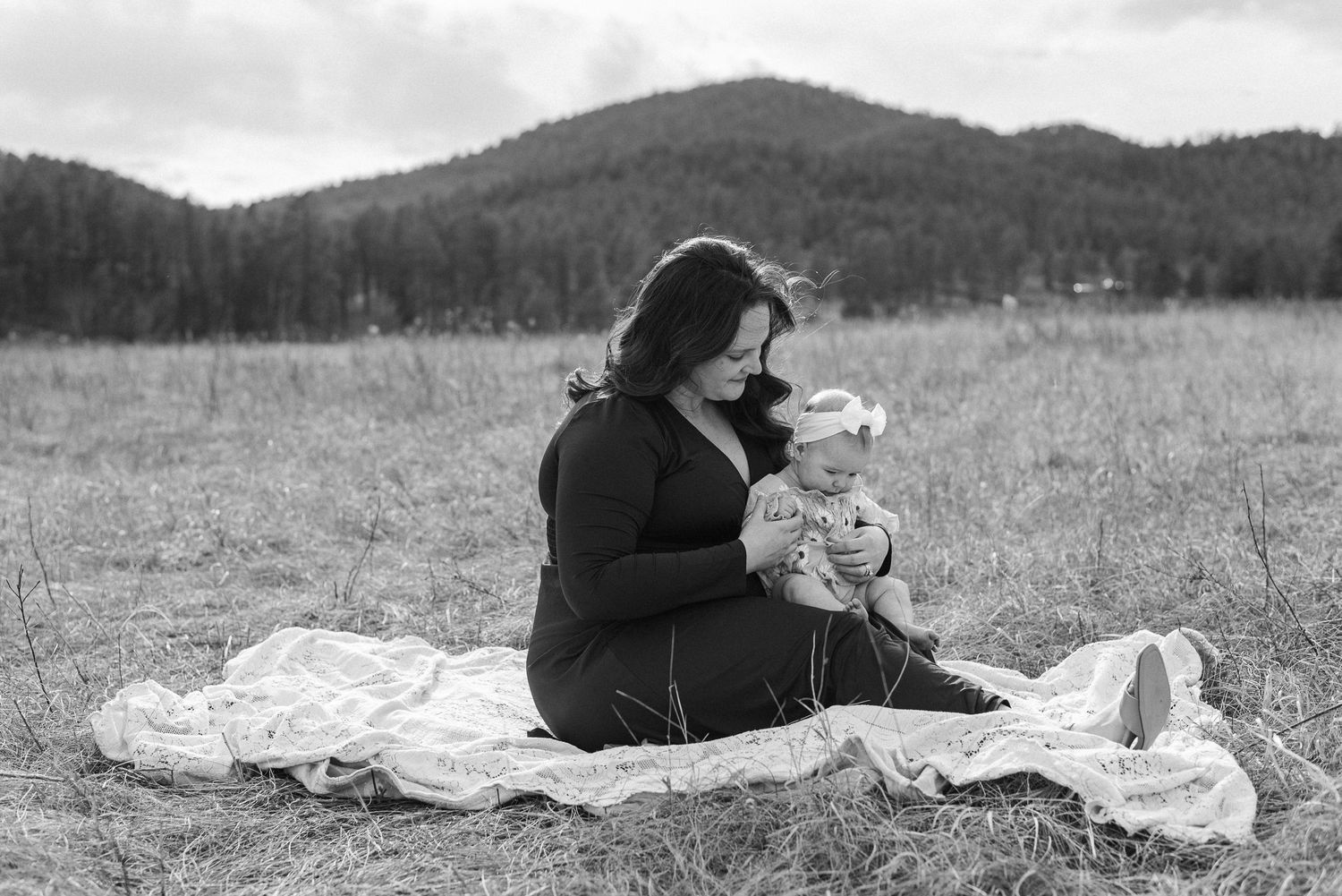 Parent and child sharing tender moments on blanket in mountain meadow.