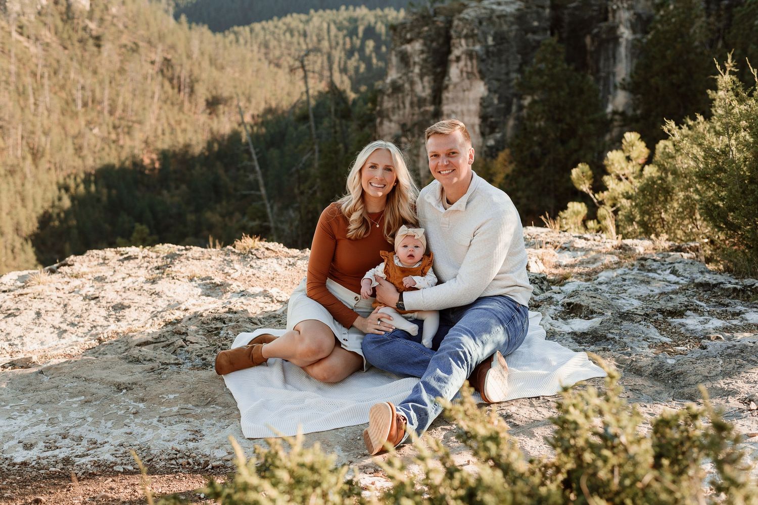 A couple sits on a rocky mountain ledge during sunset, enjoying scenic mountain views in the wilderness.