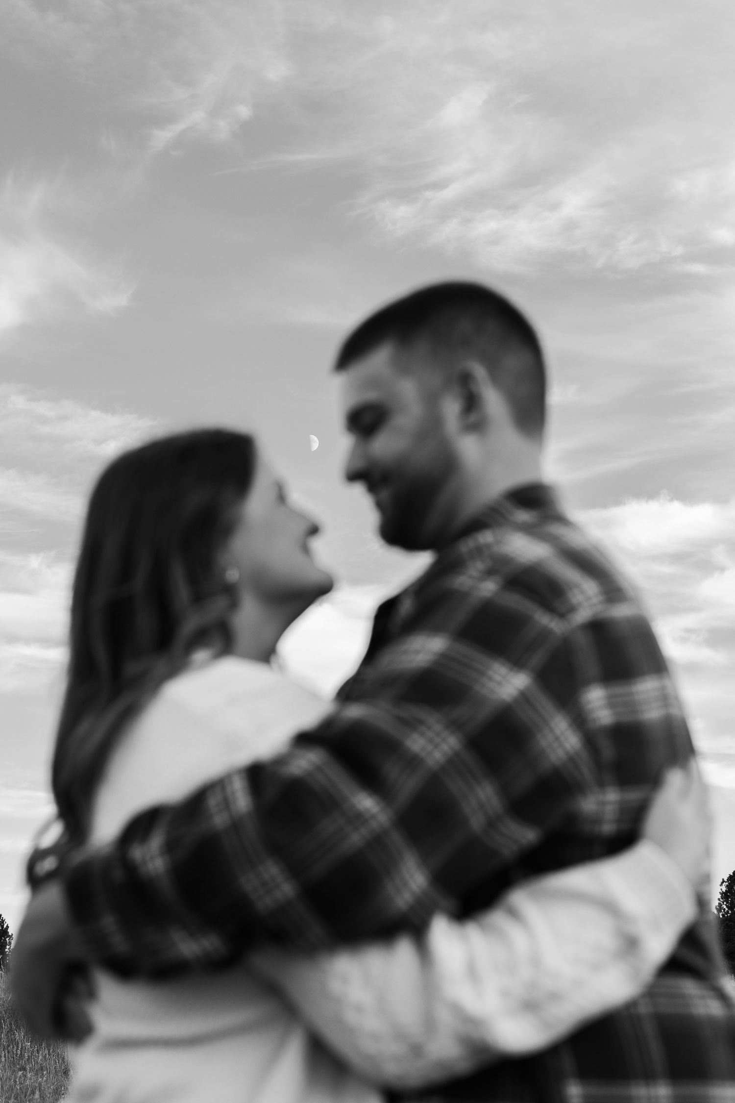 Black and white intimate portrait of a couple embracing against cloudy sky.