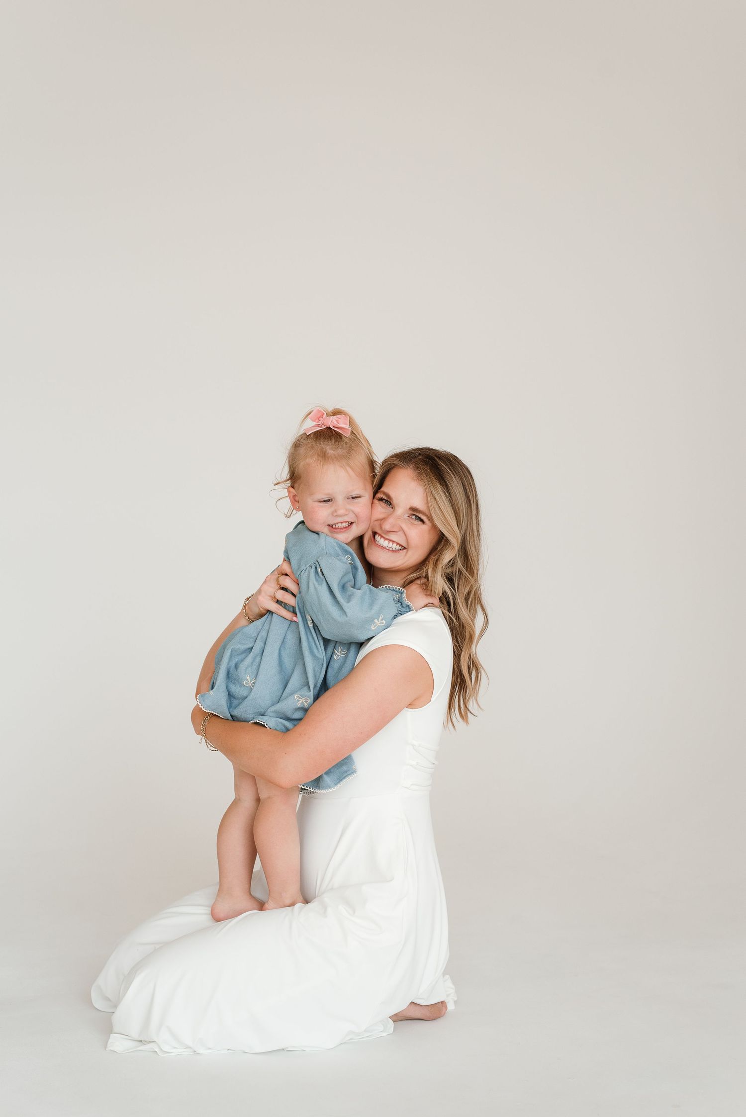 A tender portrait of a parent and child in matching light blue and white outfits against a neutral background.