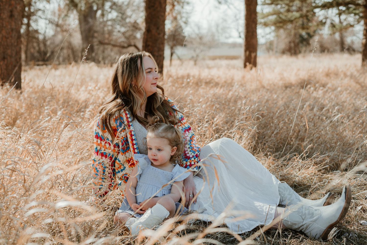 Two people embrace in a field while wearing a vibrant granny square sweater and light blue dress.