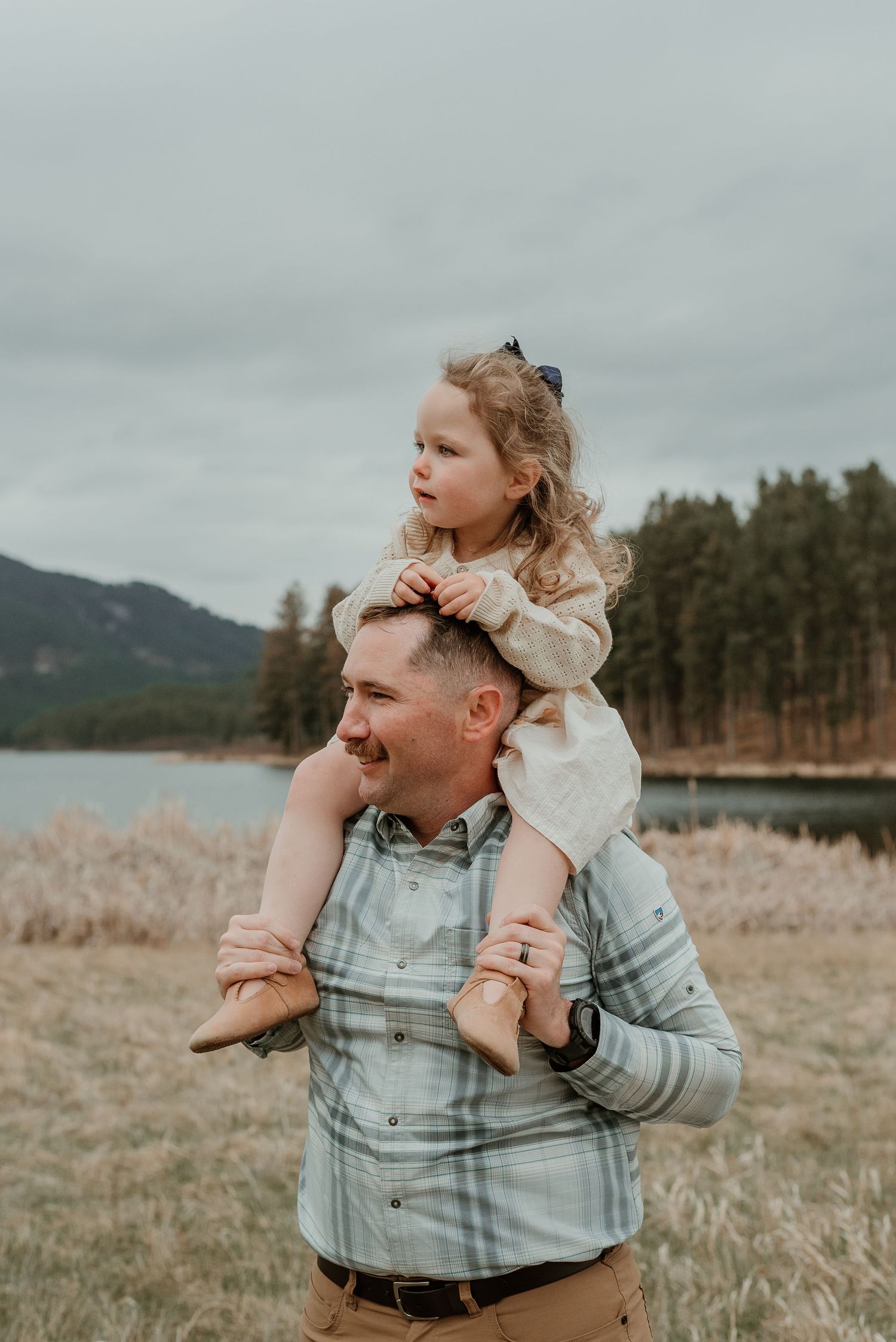 A joyful shoulder ride moment captured against a scenic mountain lake backdrop.