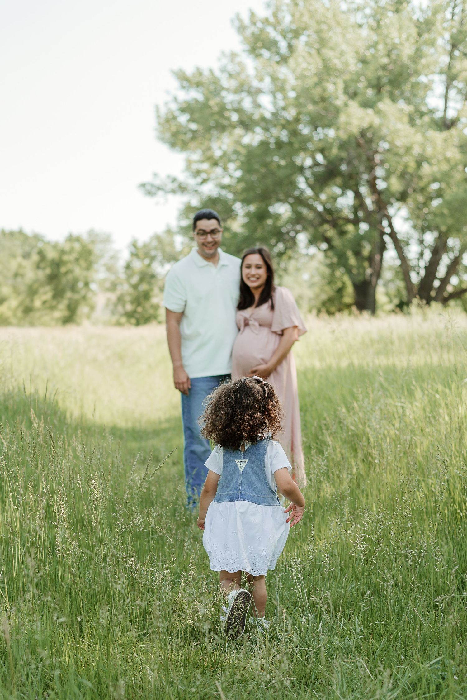 A family poses together in a grassy field on a sunny afternoon.