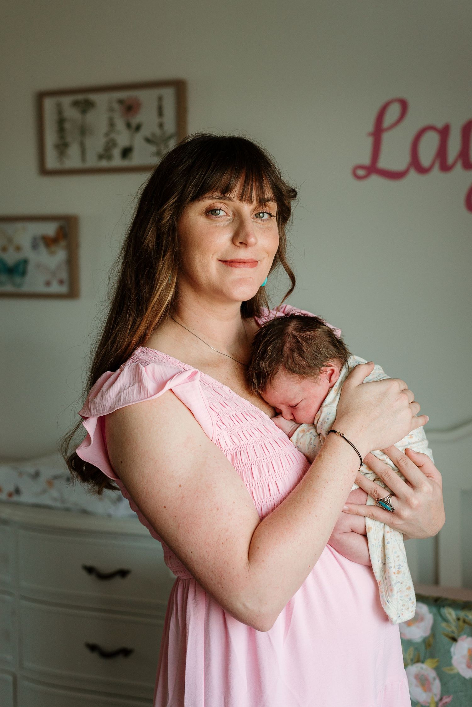 A tender moment captured in soft light as a mother in a pink dress cradles and comforts her newborn baby.