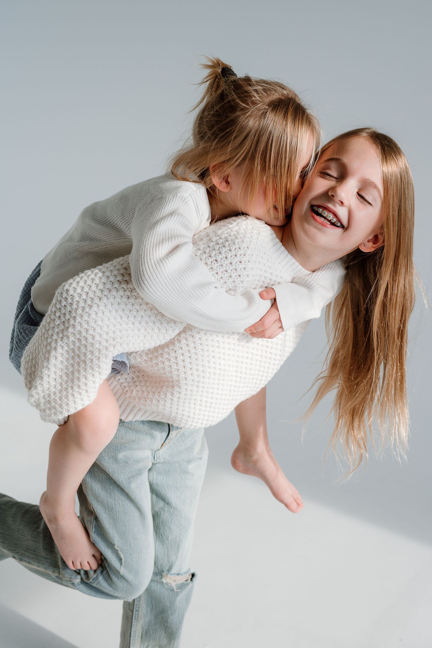 Sequence of four photos showing playful movement in a white sweater and light jeans against a white background.