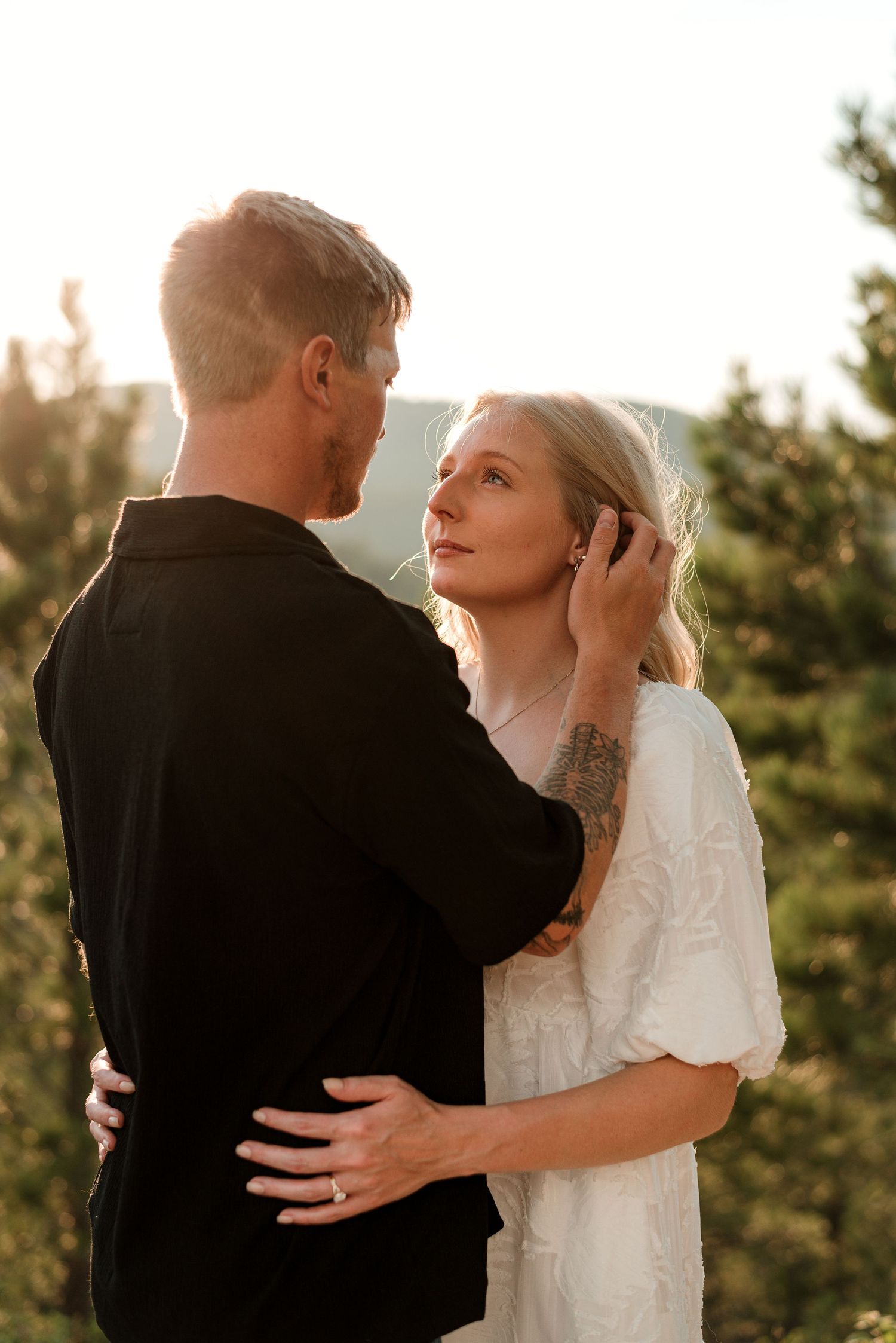 Intimate sunset portrait of a couple in white dress and black shirt against a forest backdrop.