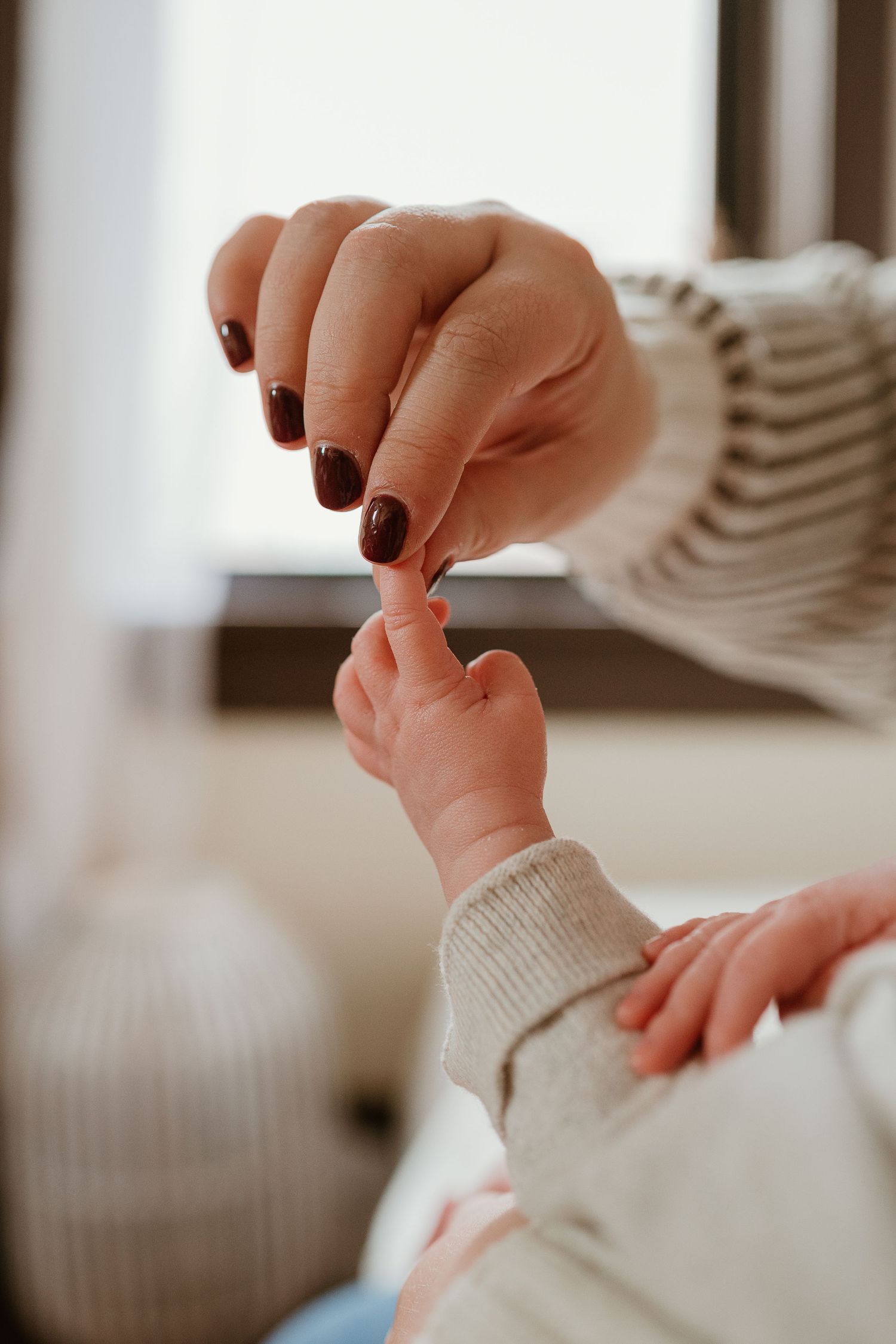 Close-up of tiny baby feet being gently held by hands with dark nail polish.