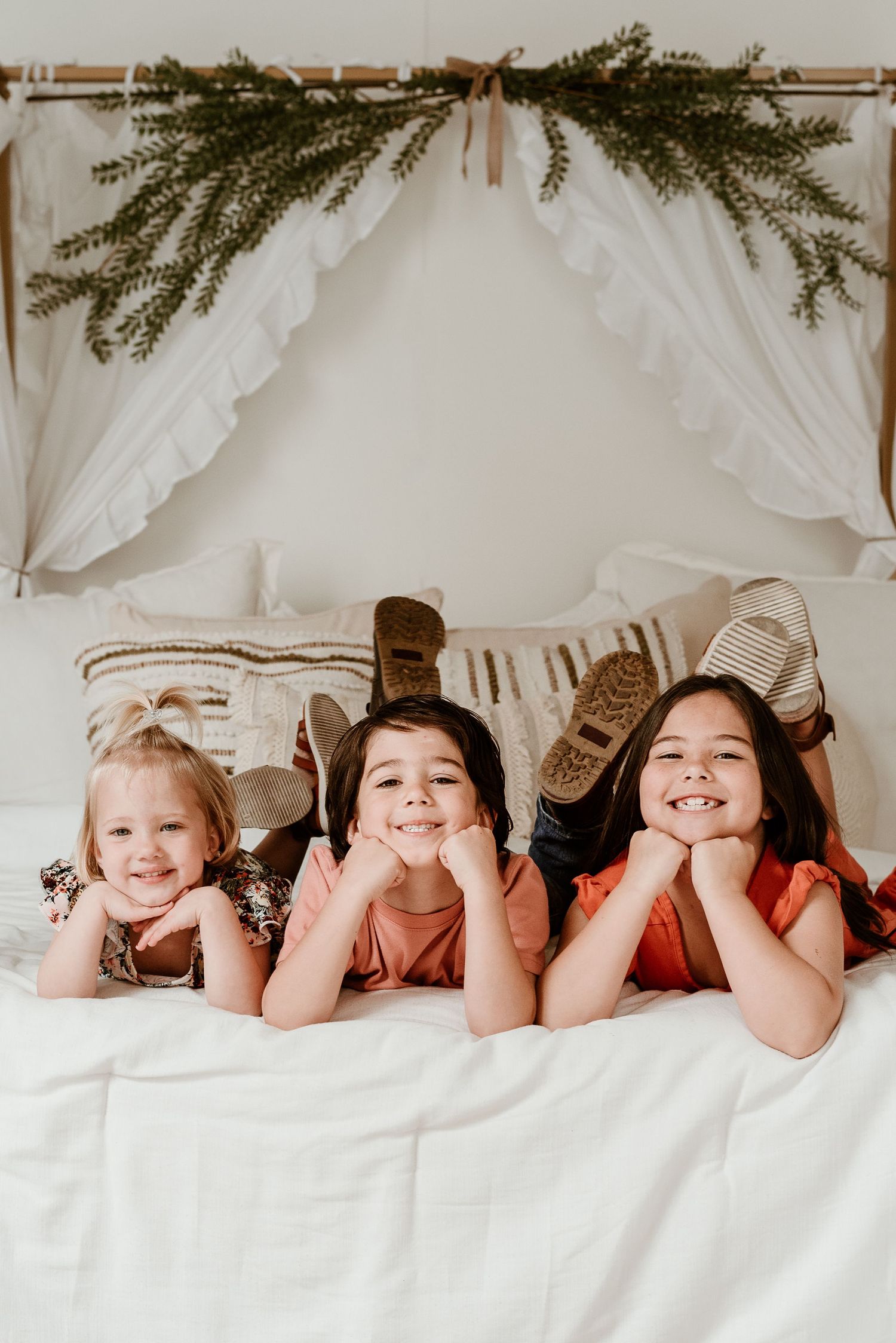 Family members lying together under white bedding with greenery decoration above.