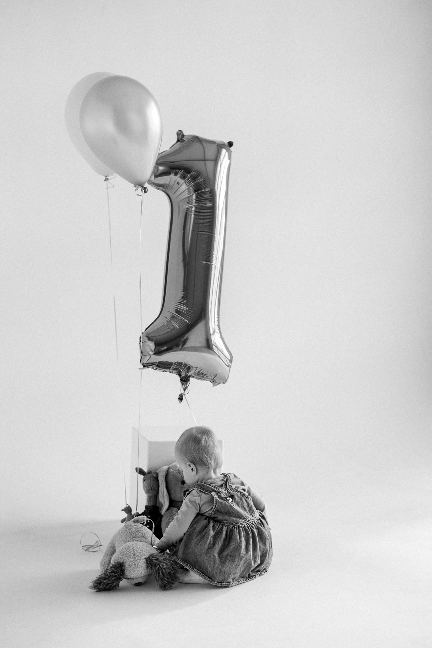 Black and white photo series showing a balloon number one with soft toys arranged in minimalist style.
