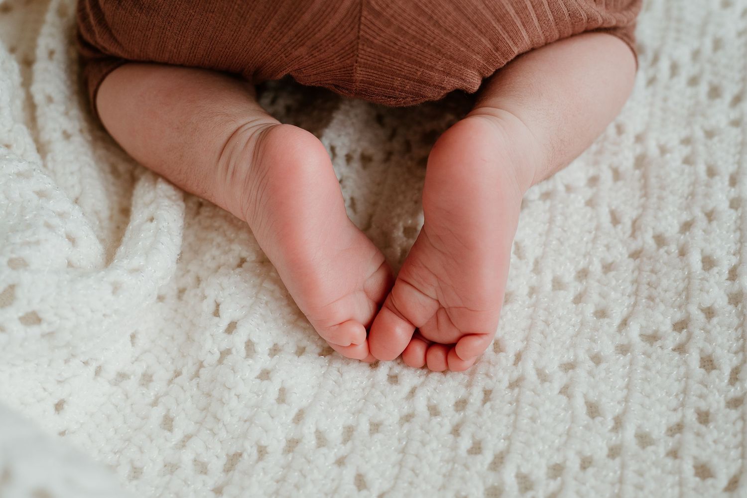 Close-up view of tiny baby feet with delicate toes against a white textured background.