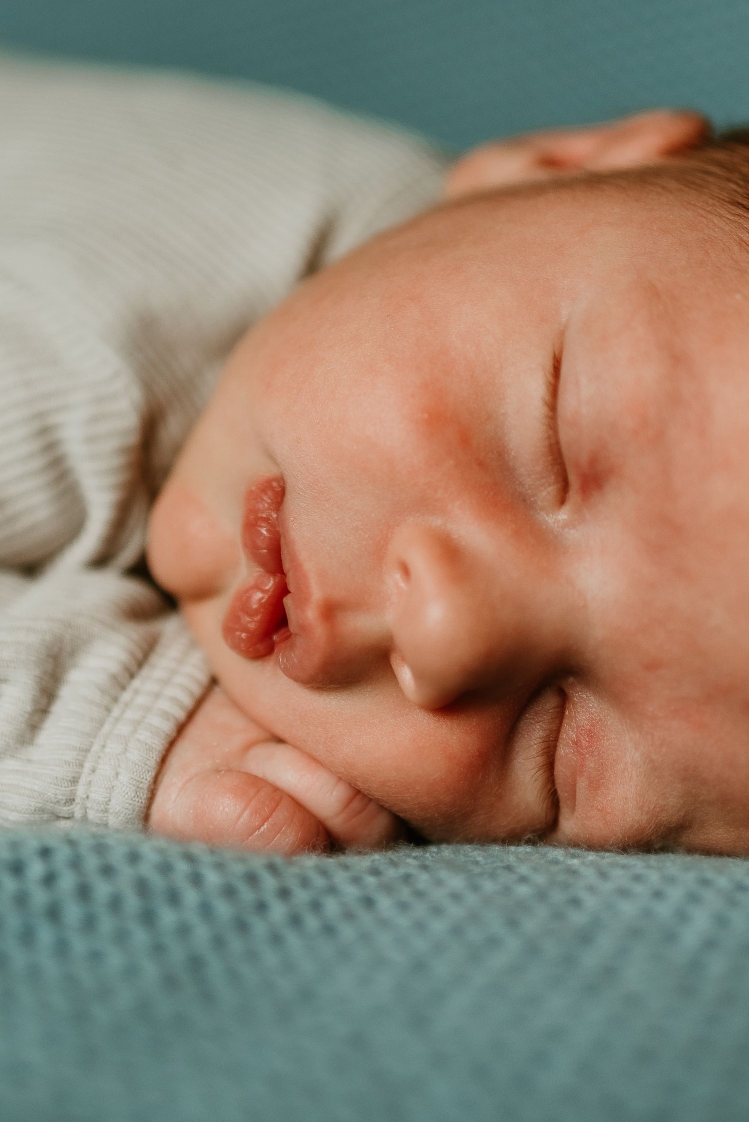 Close-up macro photography of a sleeping baby's face against a teal and white textured background.