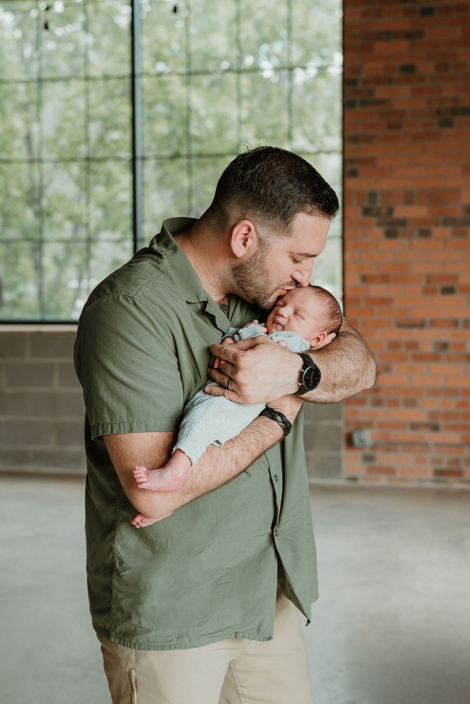 An emotional moment between a parent and newborn baby against a brick wall backdrop.