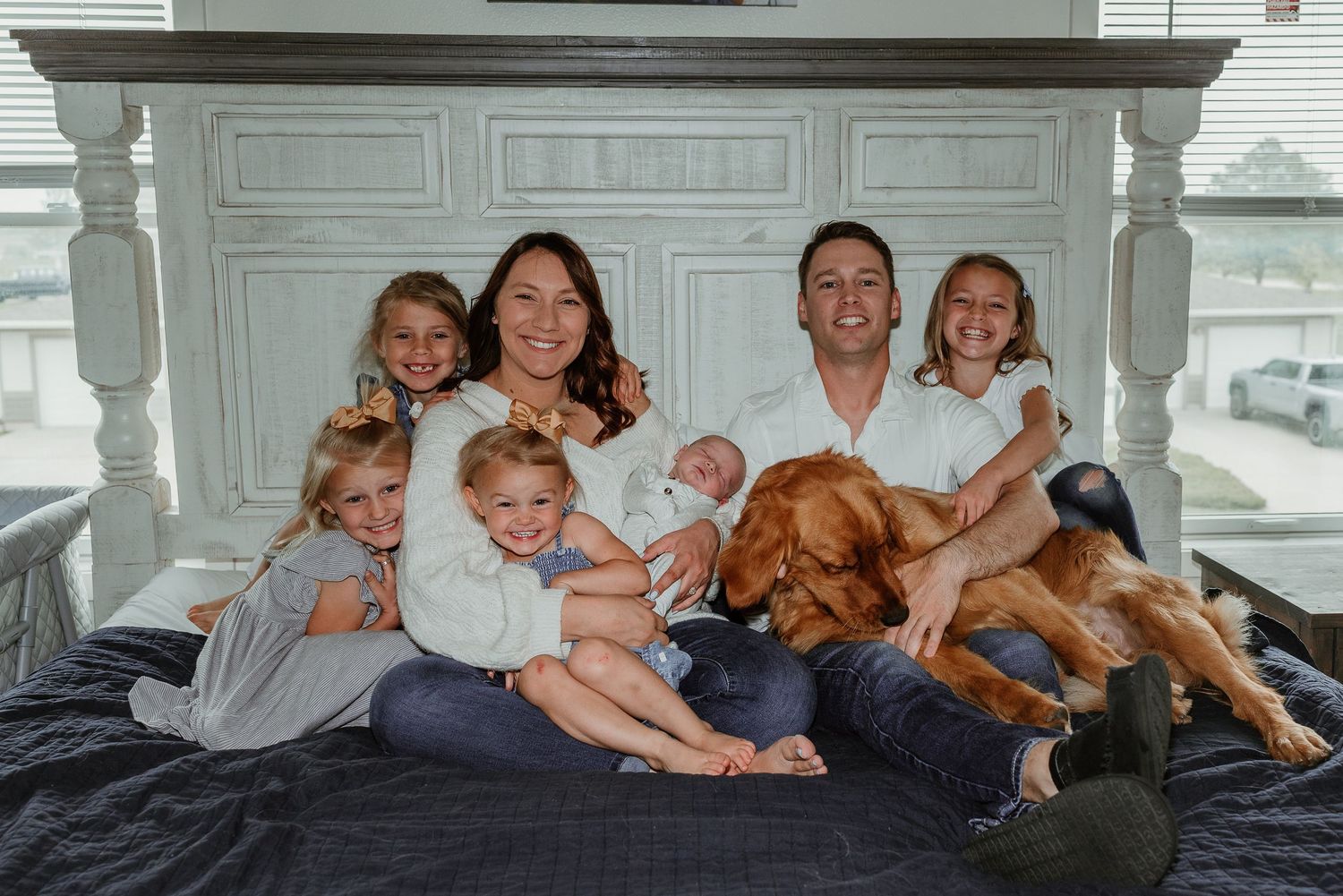 A family relaxes together on a bed with their pets.