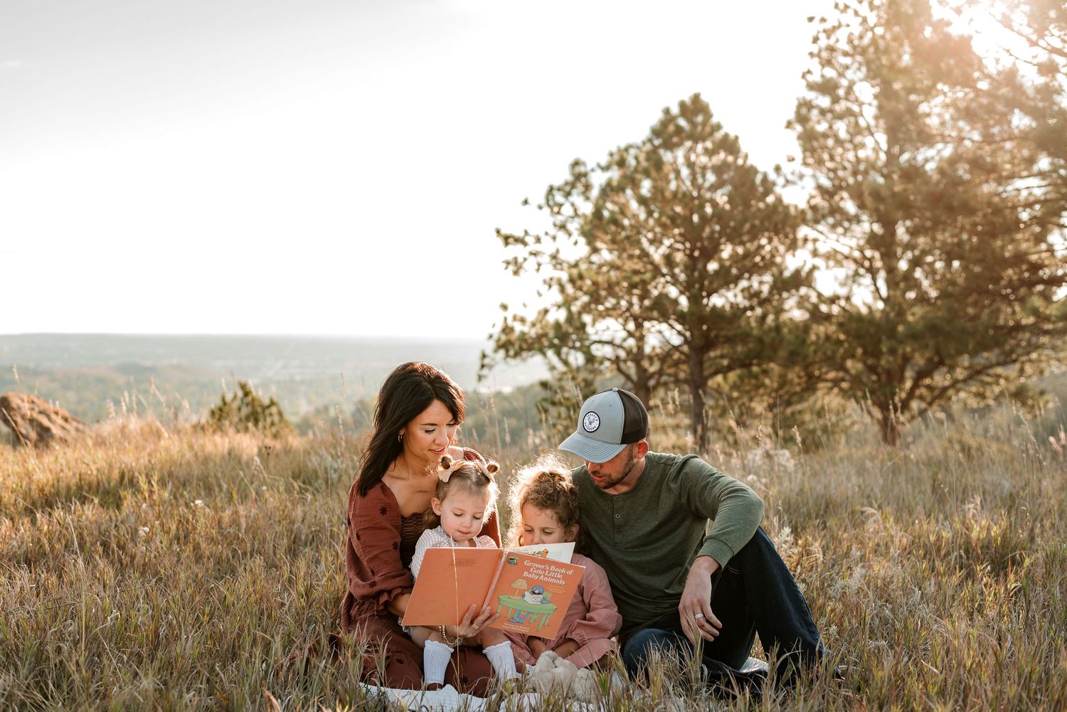 A couple embraces in a golden field during sunset while wearing casual outdoor attire.