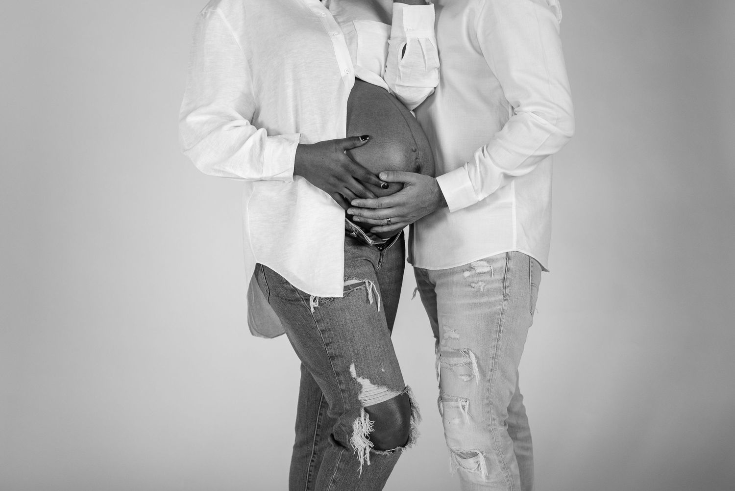 Black and white maternity photo of couple in matching white shirts holding pregnant belly.