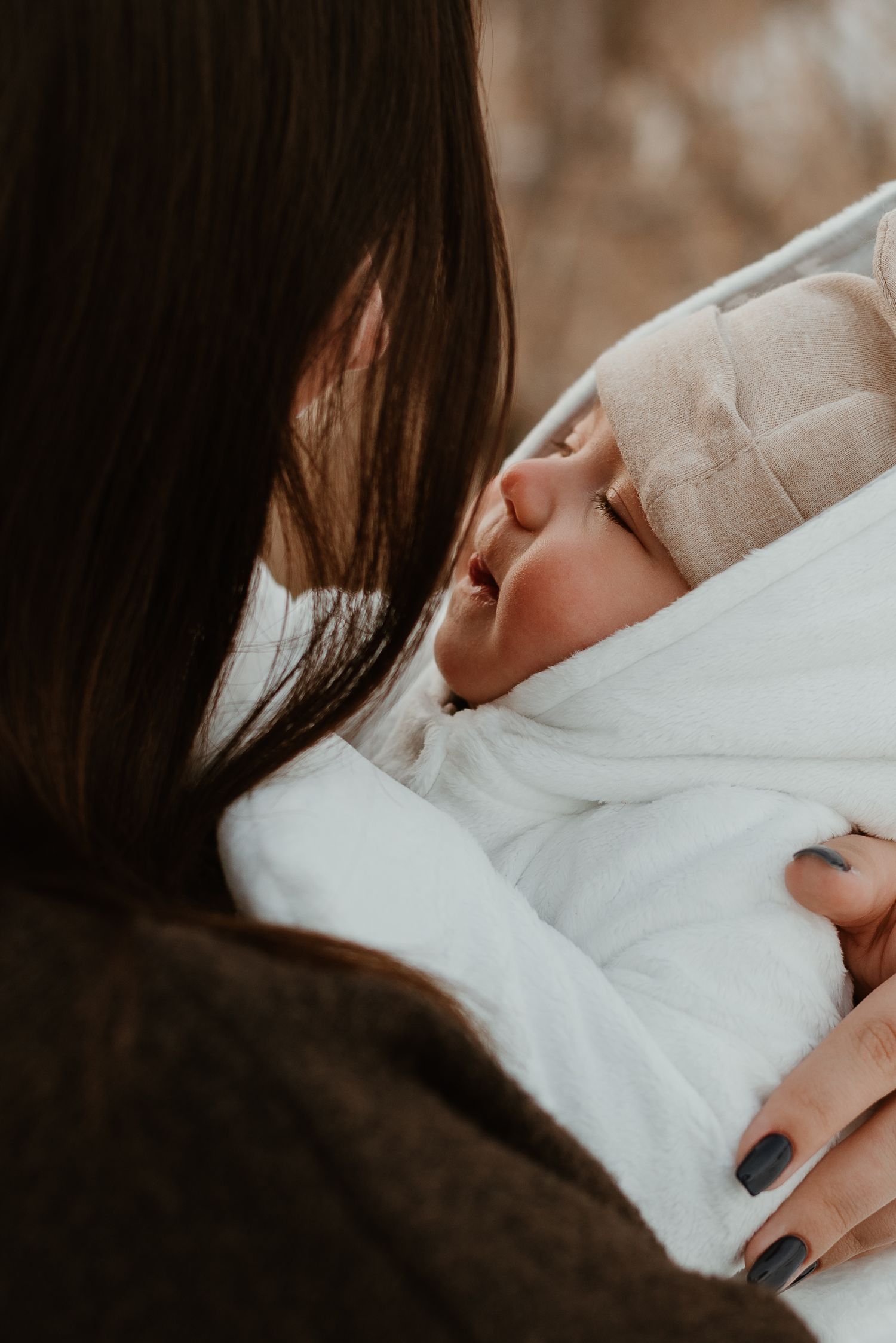 Close-up of a newborn baby being cradled in white blankets with dark painted nails visible.