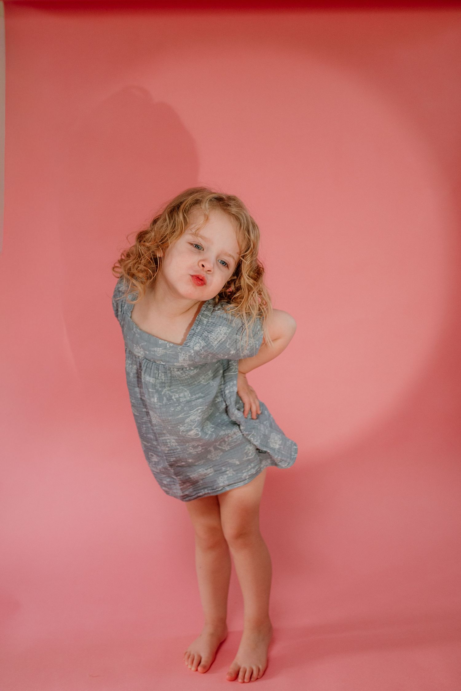 A series of four artistic portraits against a pink backdrop showing a person in a gray dress with dynamic movement poses.