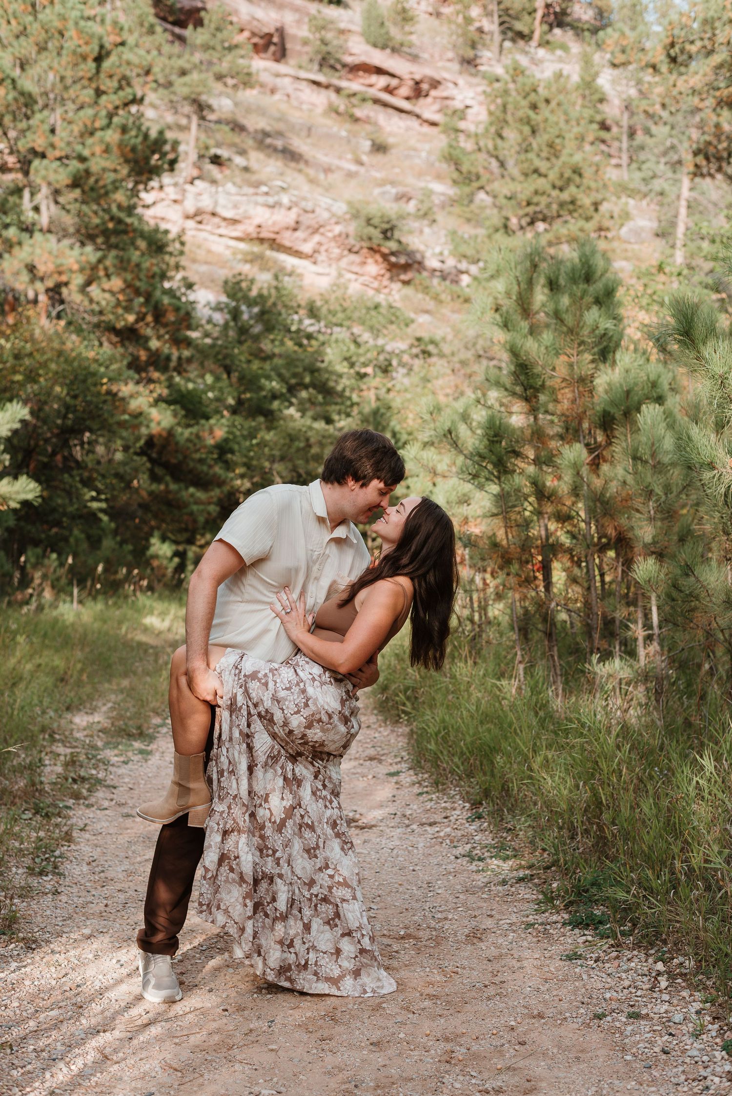 Couple sharing intimate moments along a dirt path with evergreen trees in the background.