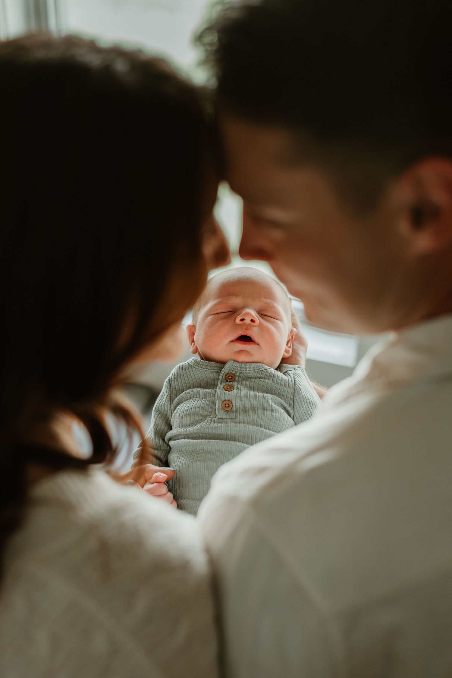 A sleeping newborn baby wearing a soft gray outfit is cradled by parents.
