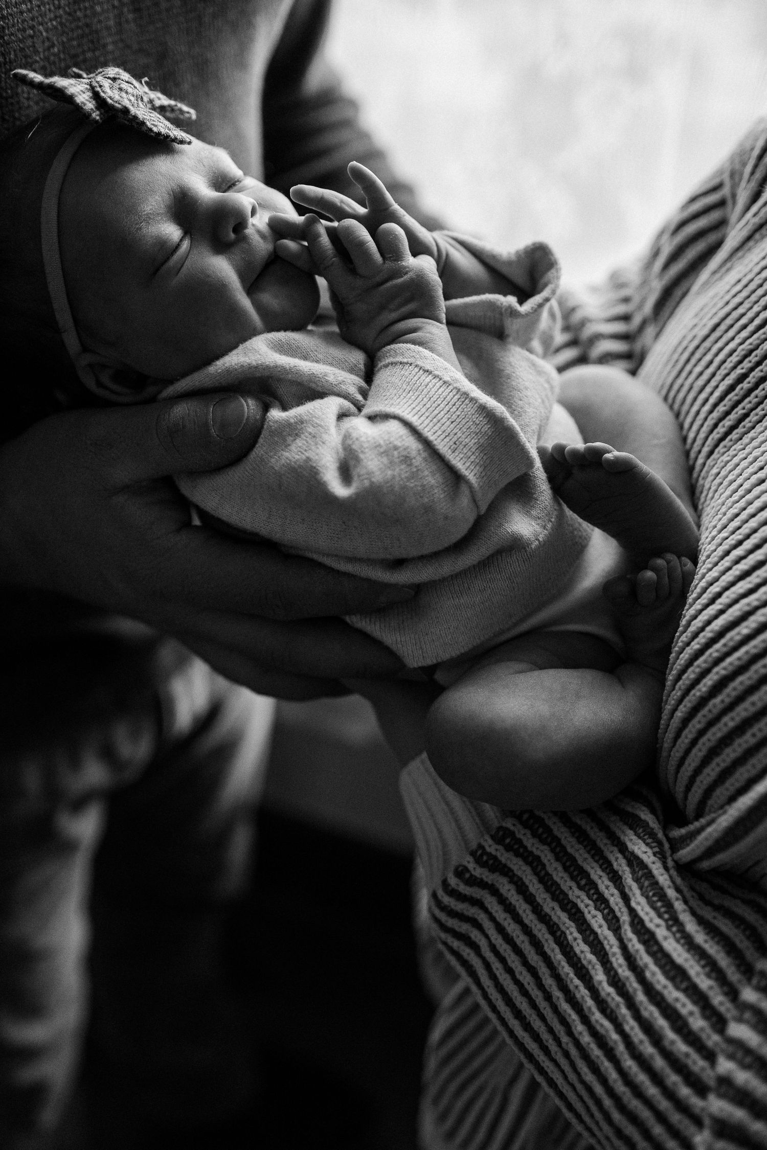 A black and white series of photos showing a newborn baby's hand grasping while resting on a striped fabric.