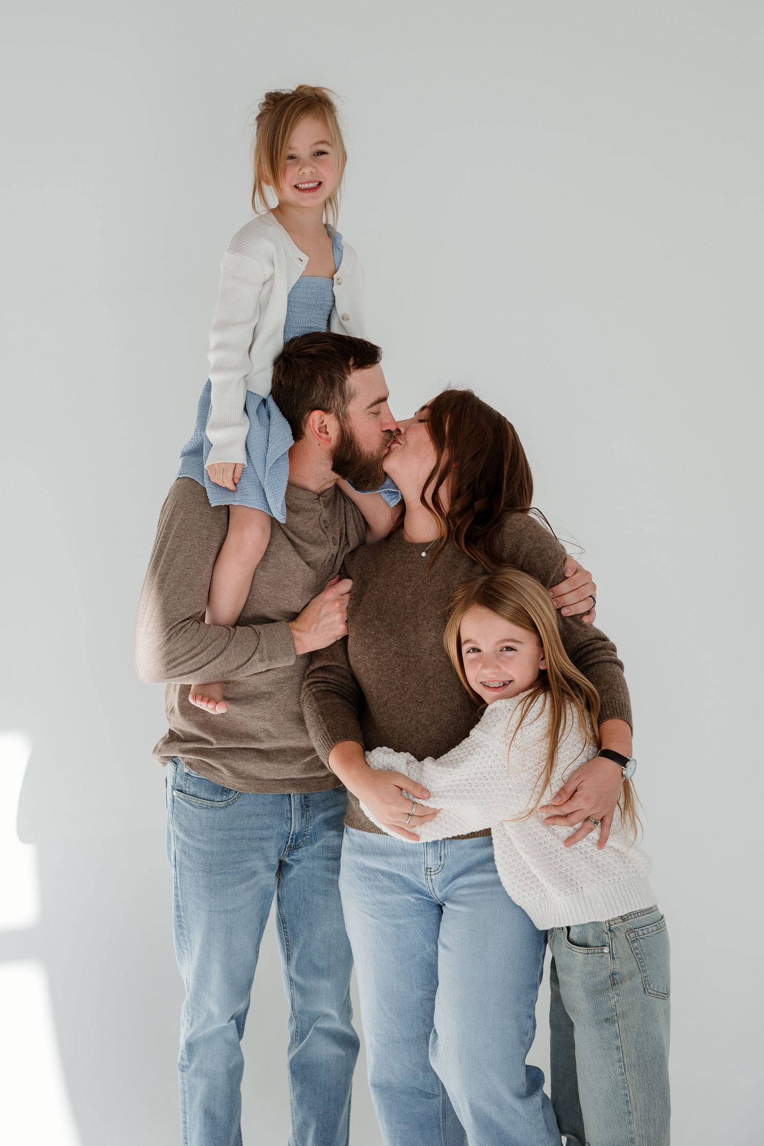 A family of four wearing casual clothing embraces in a warm group hug against a white background.