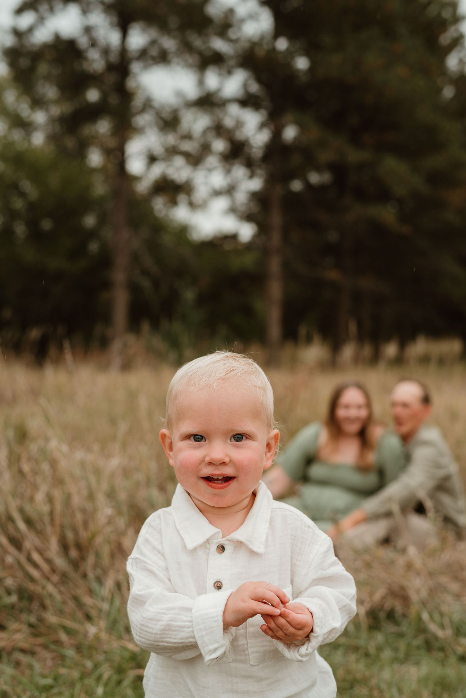 A young child wearing a white sweater sits in a grassy field on an autumn day.