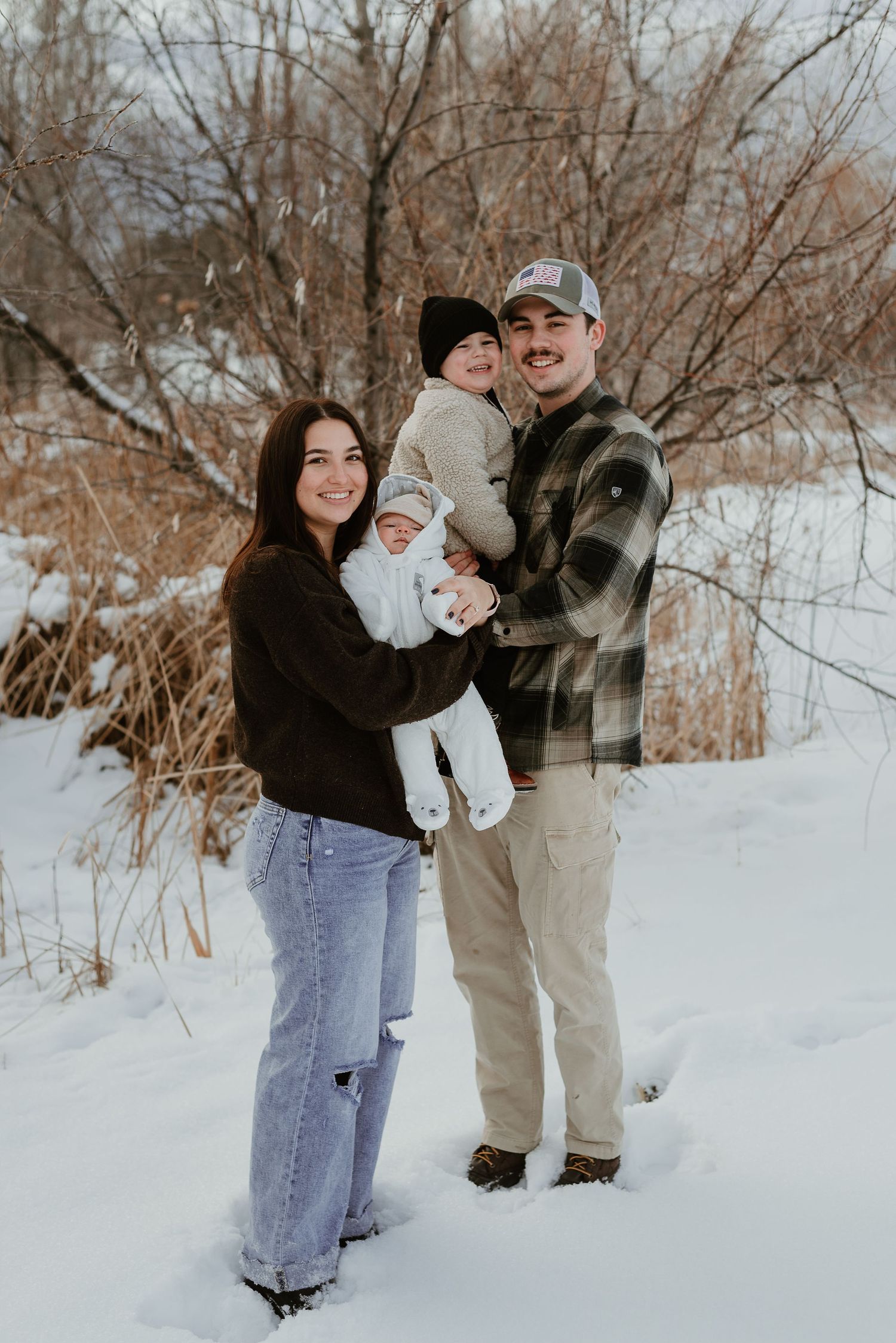 A family of three poses together in a snowy winter landscape.