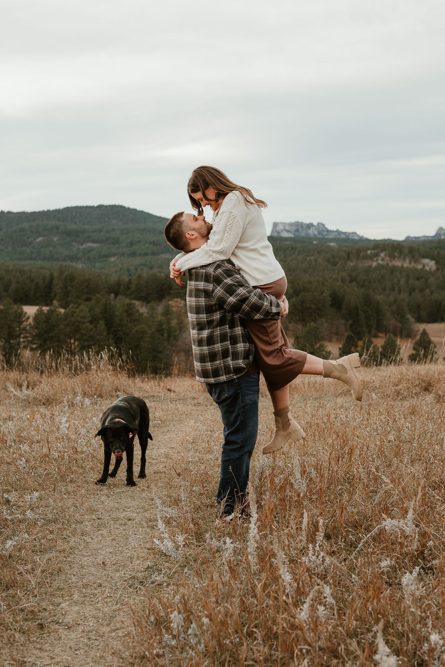Couple sharing a joyful moment in a mountain field with their black dog.