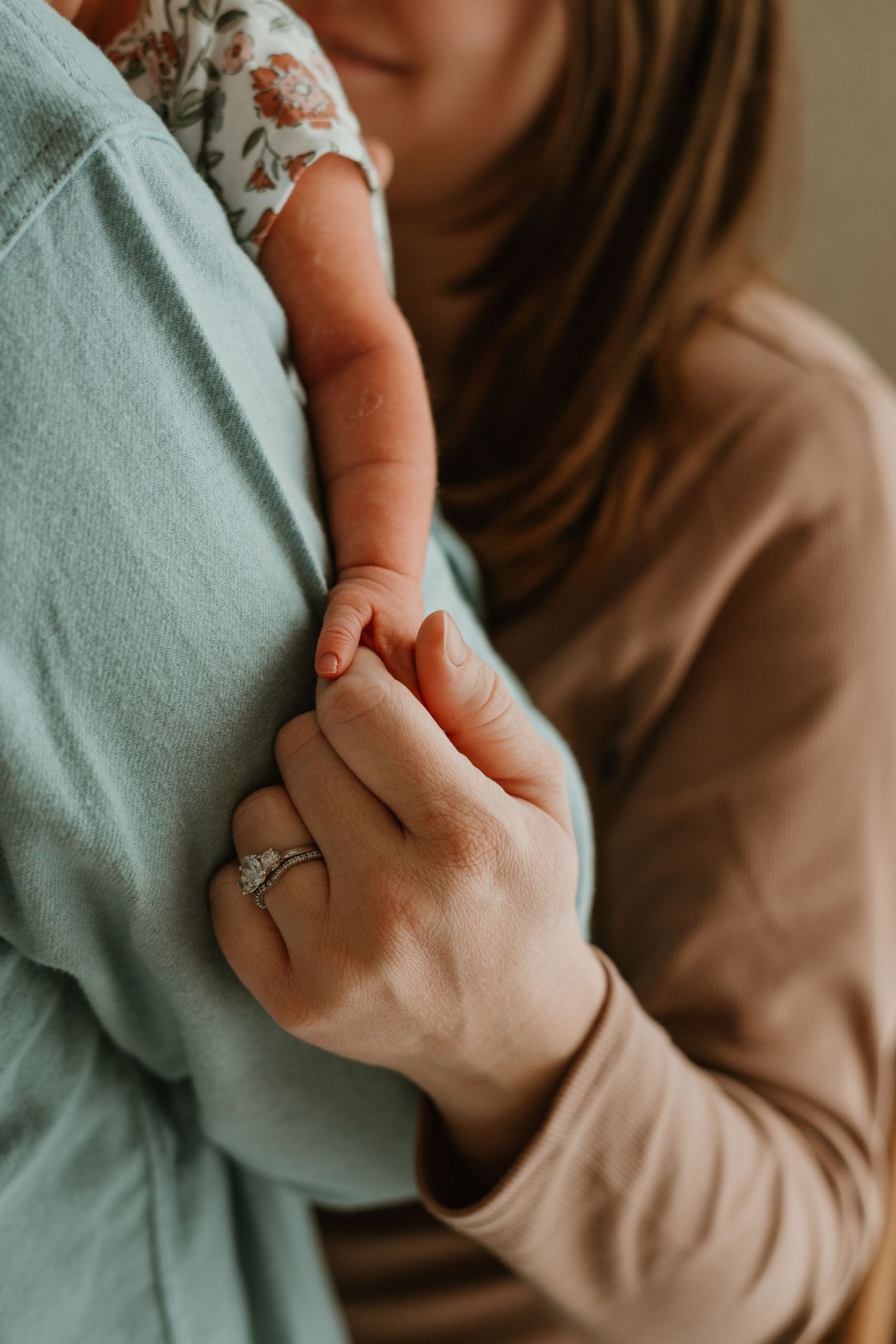 Close-up shot of hands wearing a beige sweater and mint green cardigan with an engagement ring visible.