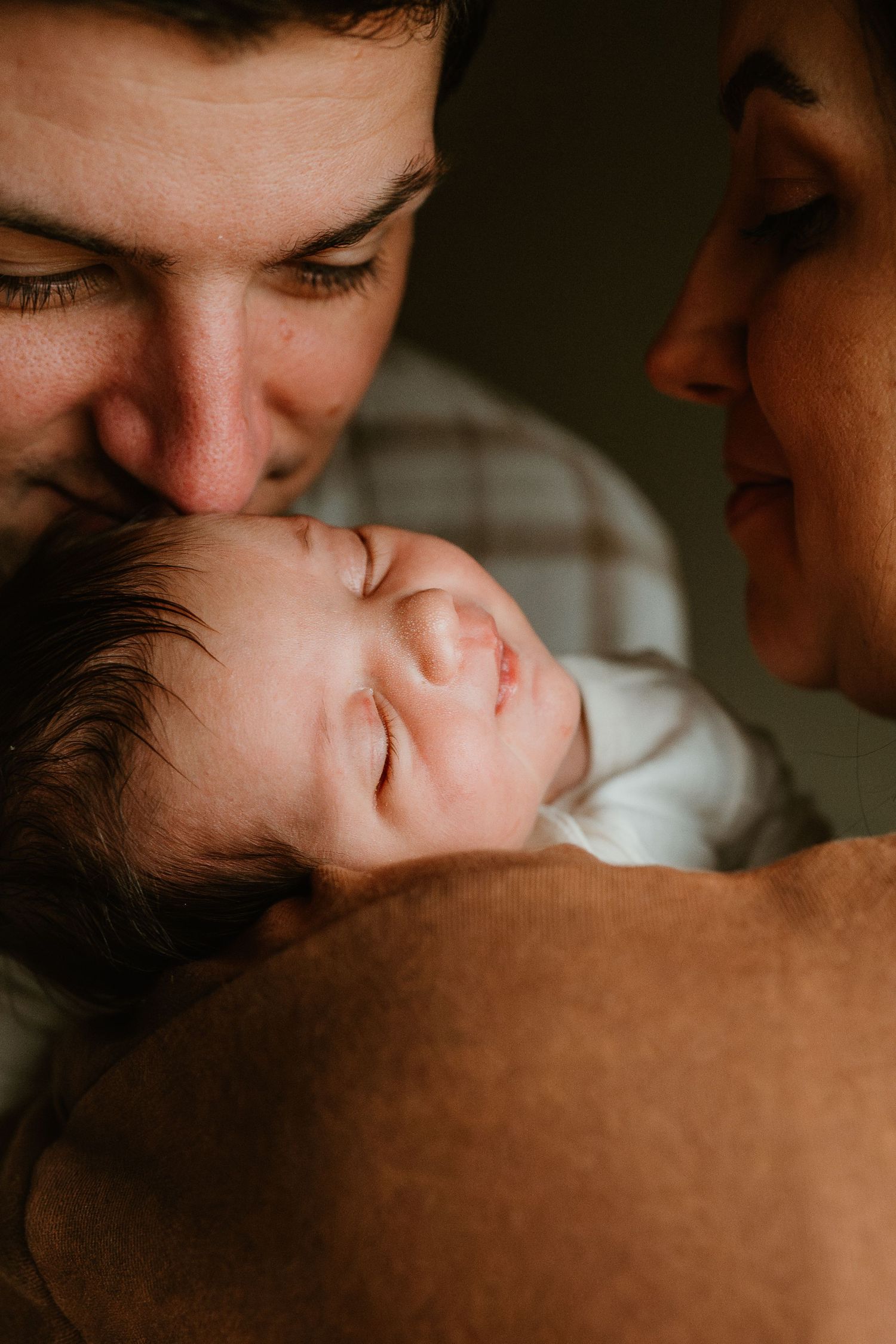Intimate close-up photos showing tender moments between parent and baby in warm, moody lighting.