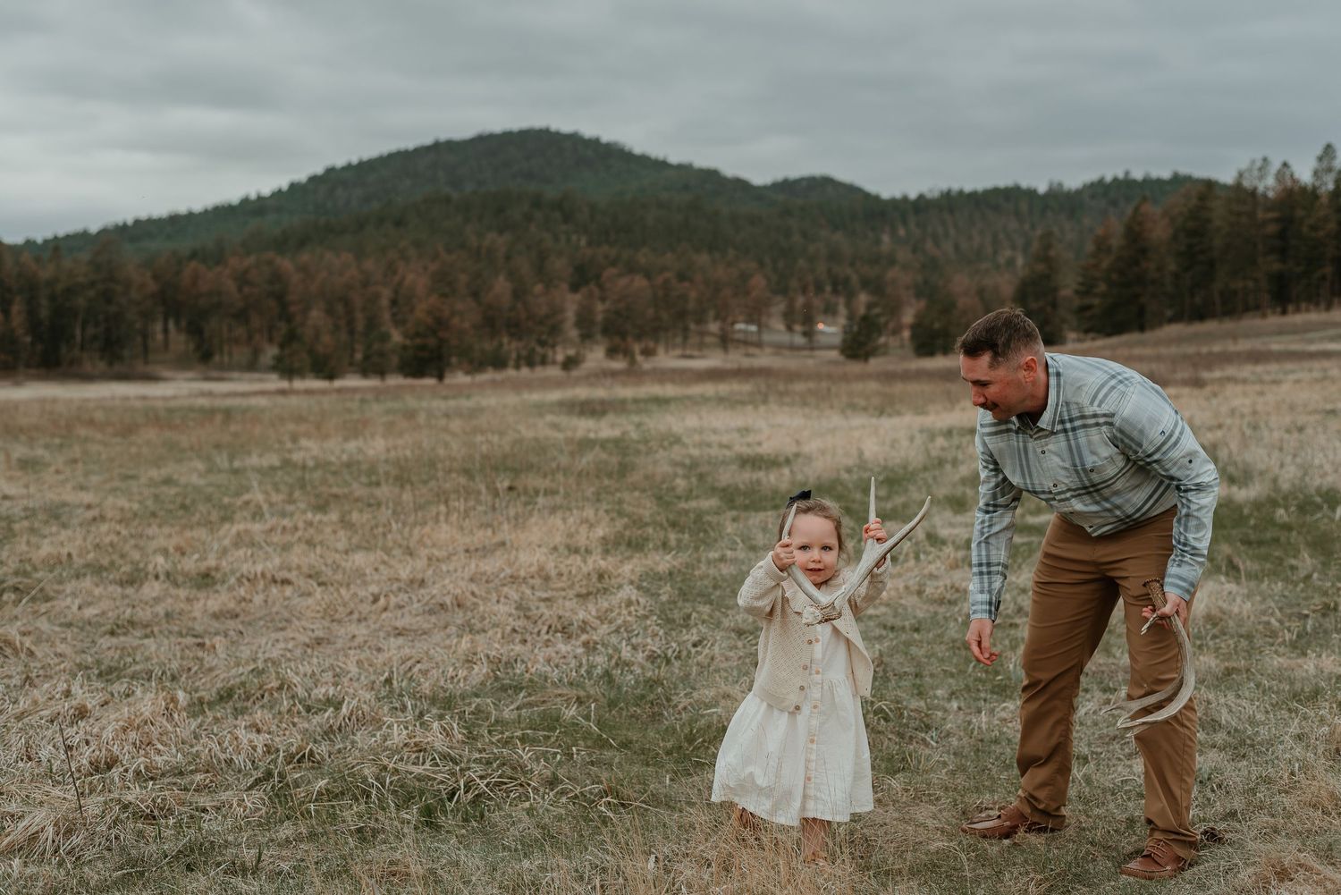 A parent and child walk together in a grassy field with mountains in the distance.