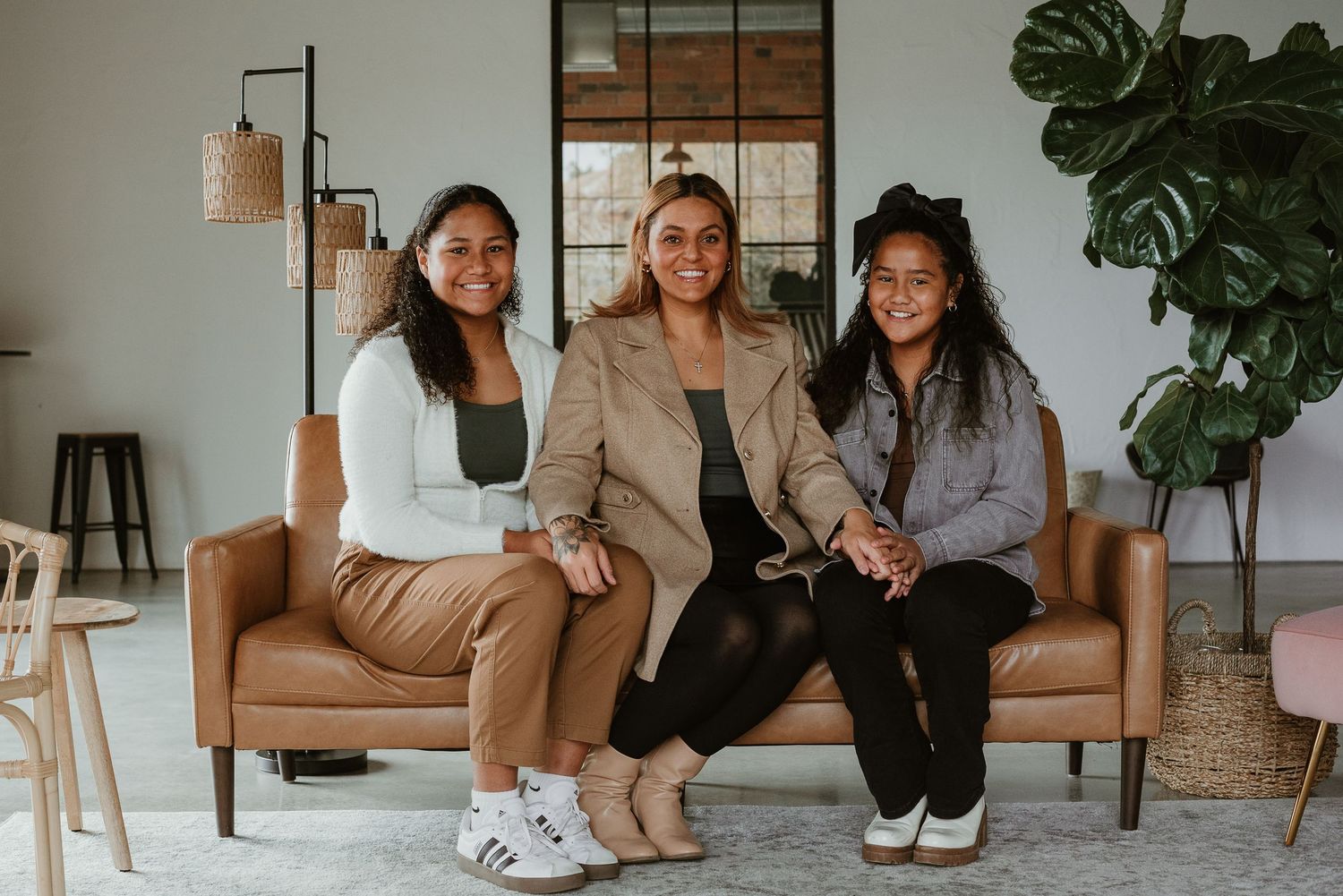 Three friends relaxing together on tan couch in modern living room with plant decor.
