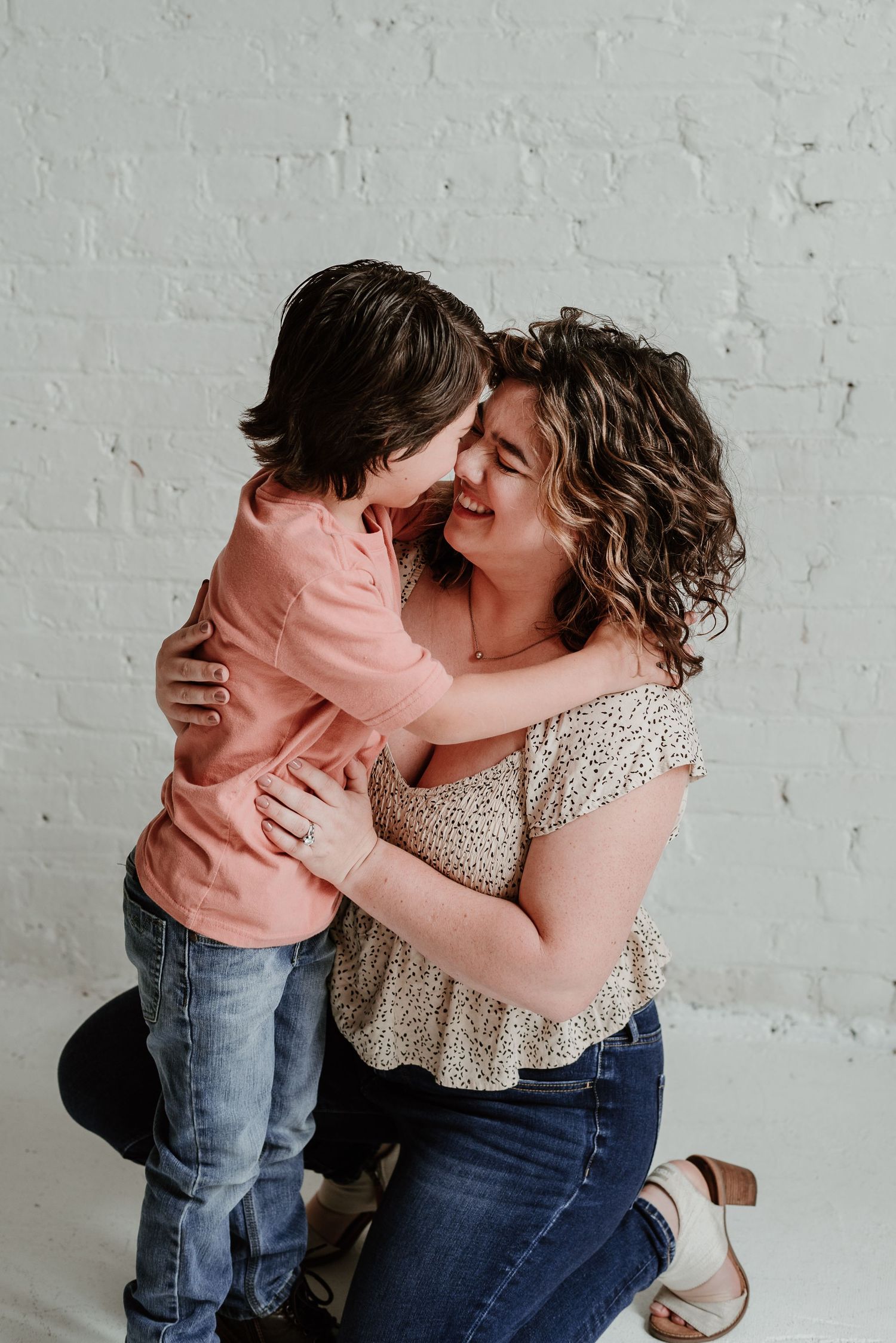 Parent and child share a tender moment of affection against a white brick wall.