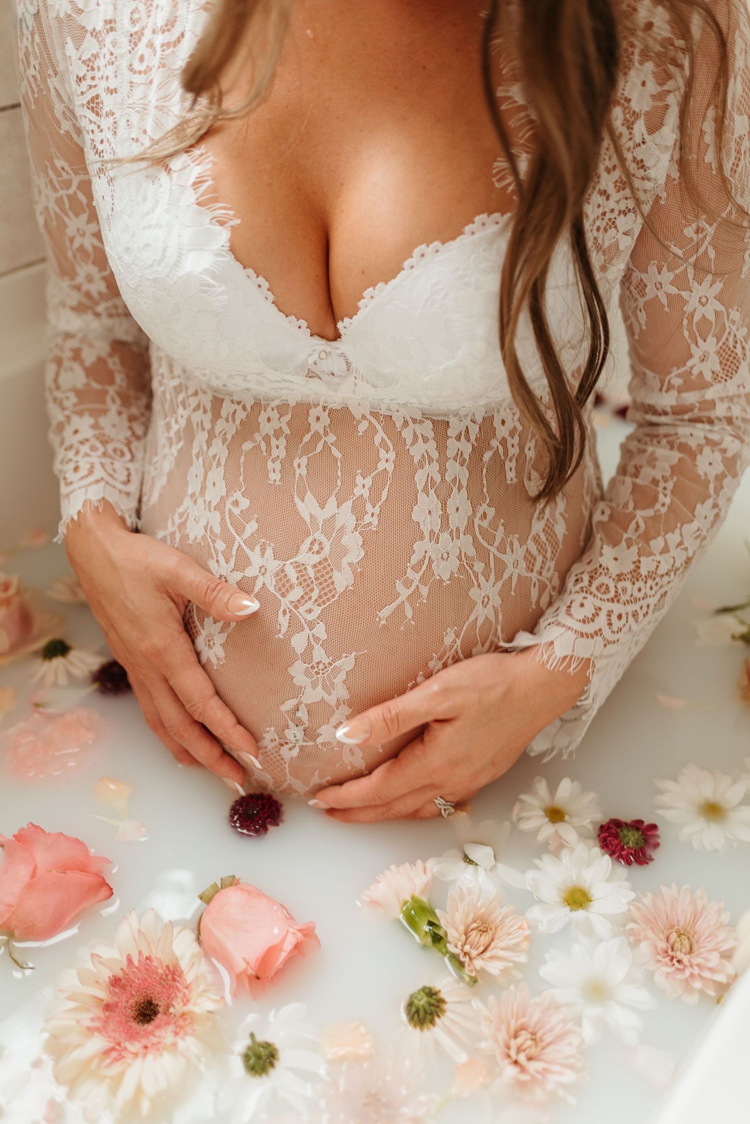 Delicate lace wedding dress bodice detail with pink and white daisies arranged below in a romantic maternity photo shoot.