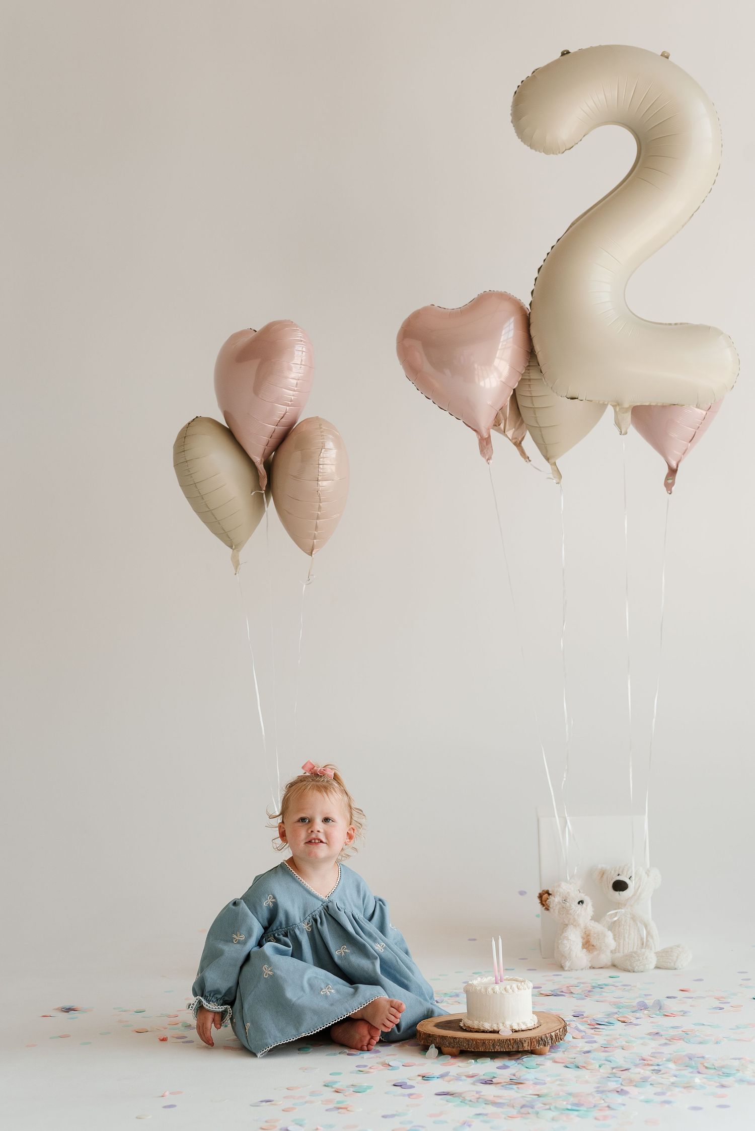 Birthday setup with number two balloon, stuffed bunny, and cake against white background.