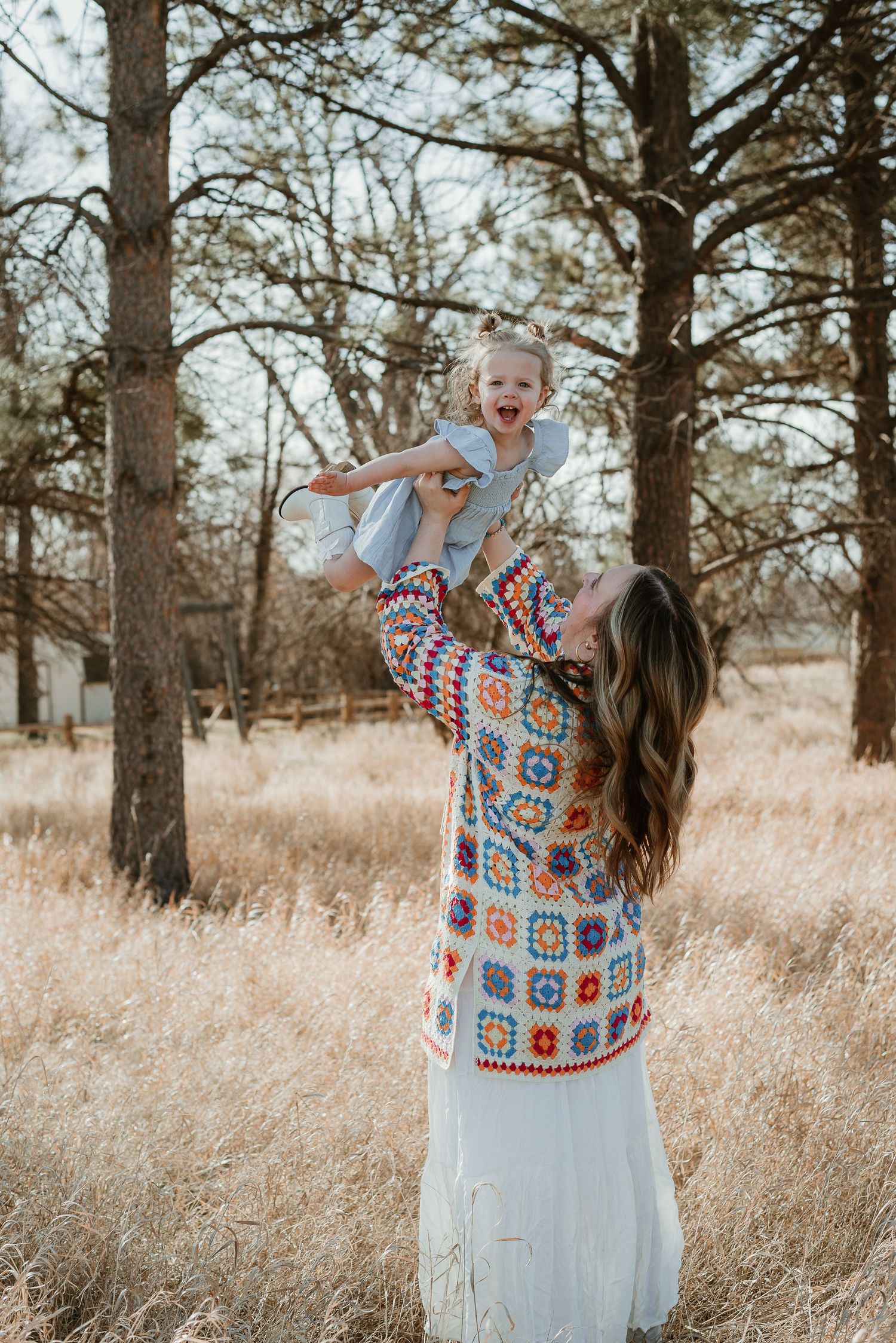 Playful outdoor photoshoot in a field with colorful crochet cardigan and white dress.