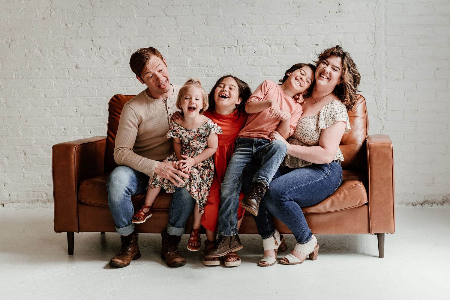 Group sitting casually on brown leather couch against white brick wall.