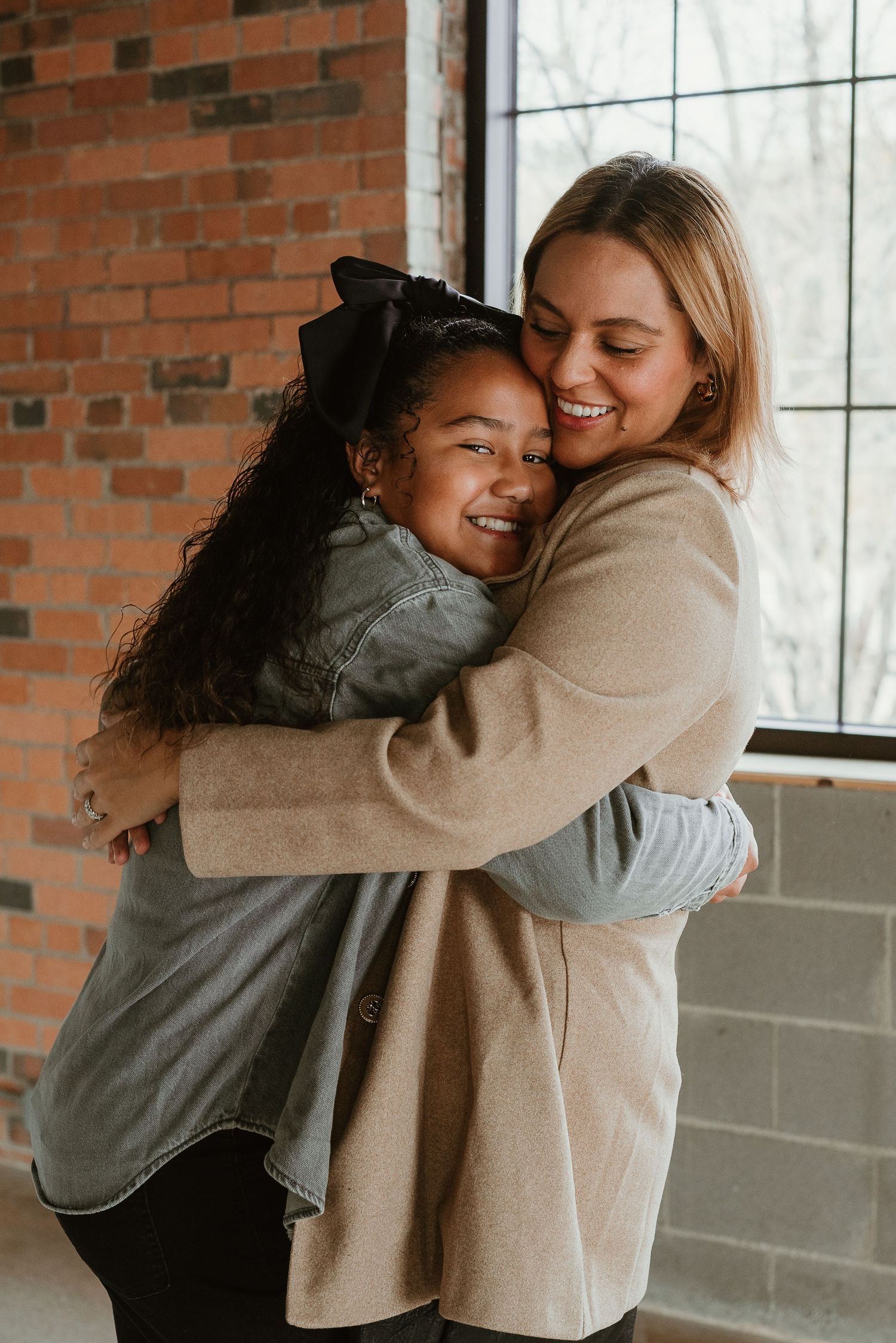 Candid moment of two people sharing warm embrace by brick window.