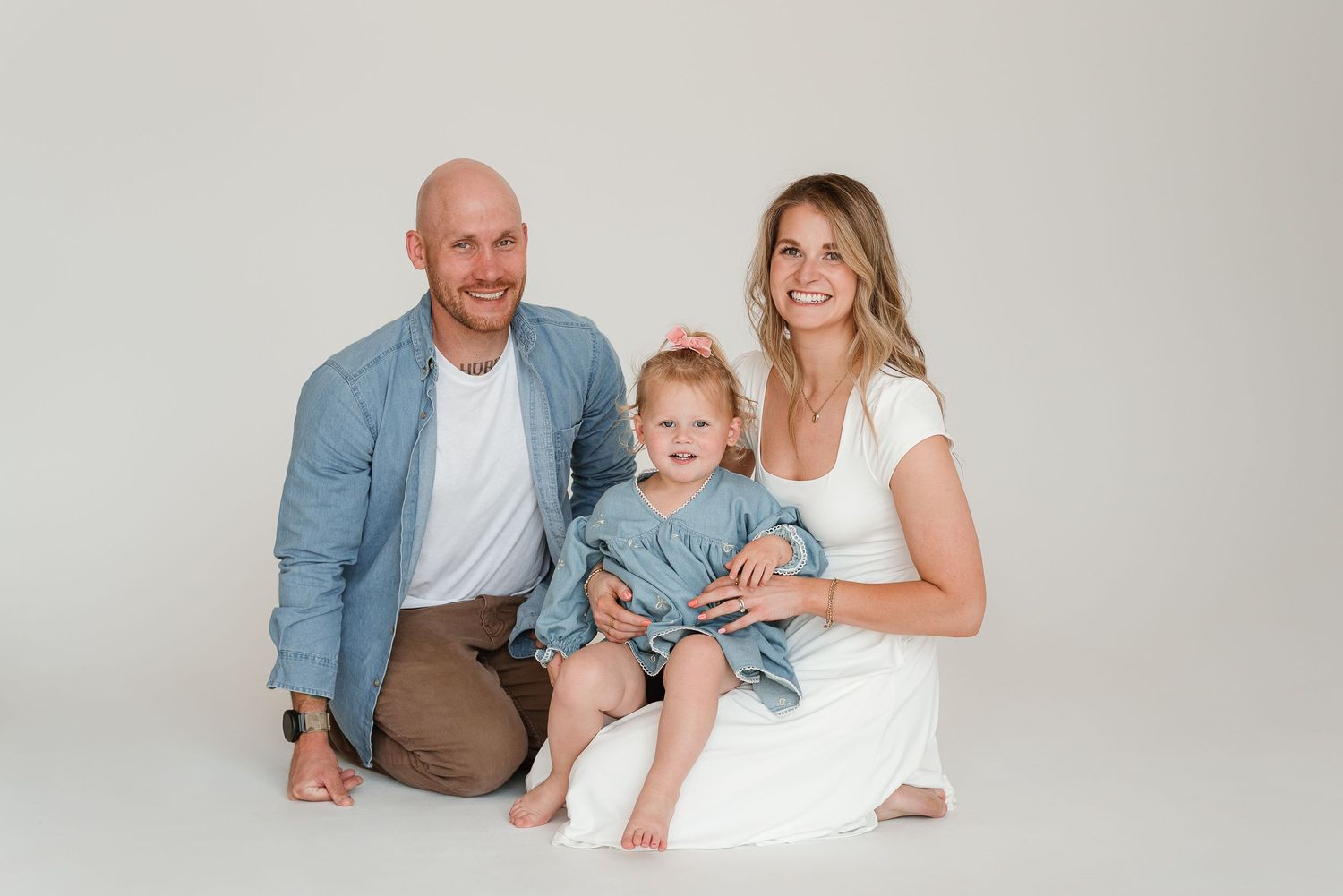 A family of three wearing coordinated blue and white outfits poses together against a light gray studio backdrop.